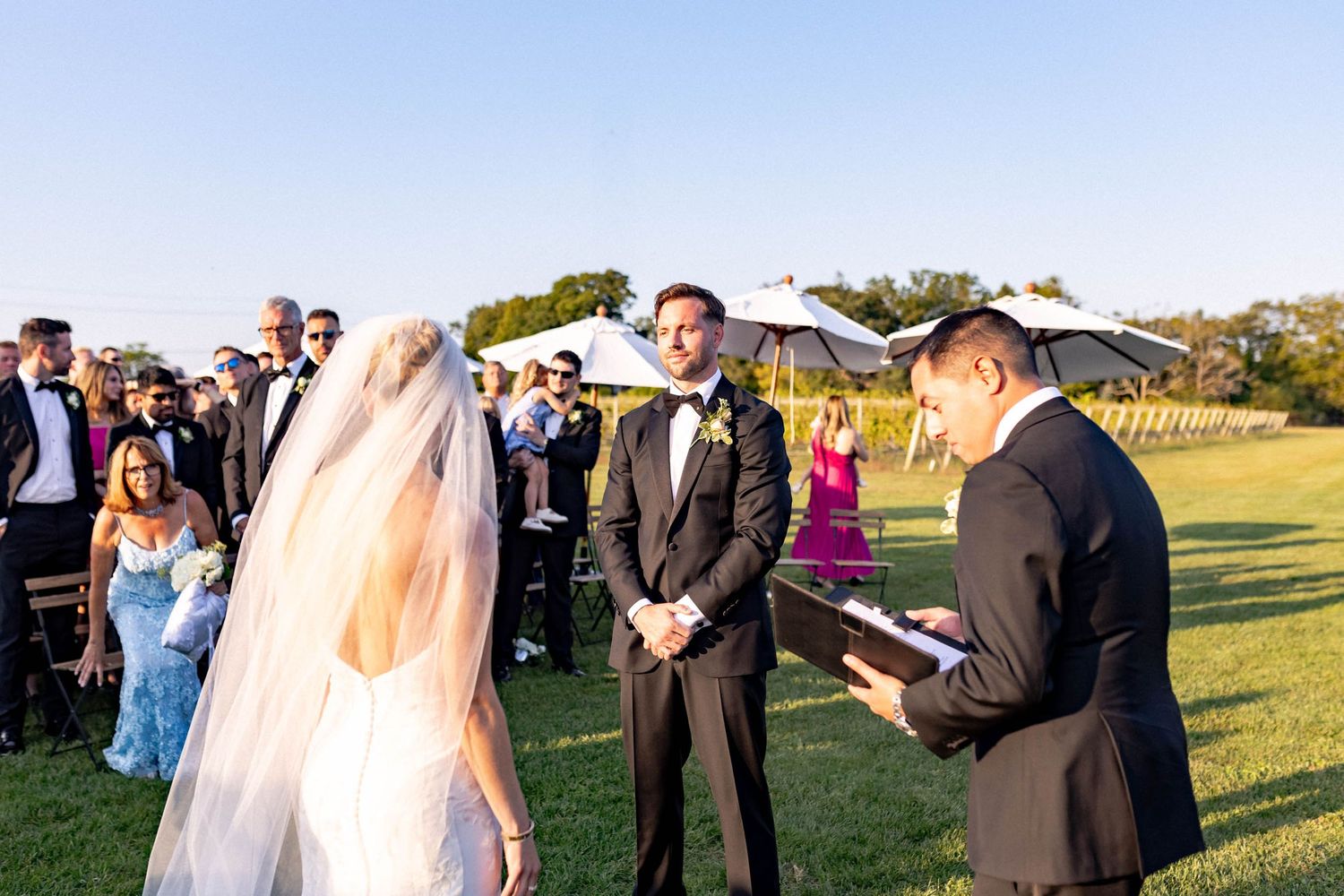 Wedding party celebrates outdoors during golden hour at a scenic vineyard ceremony.