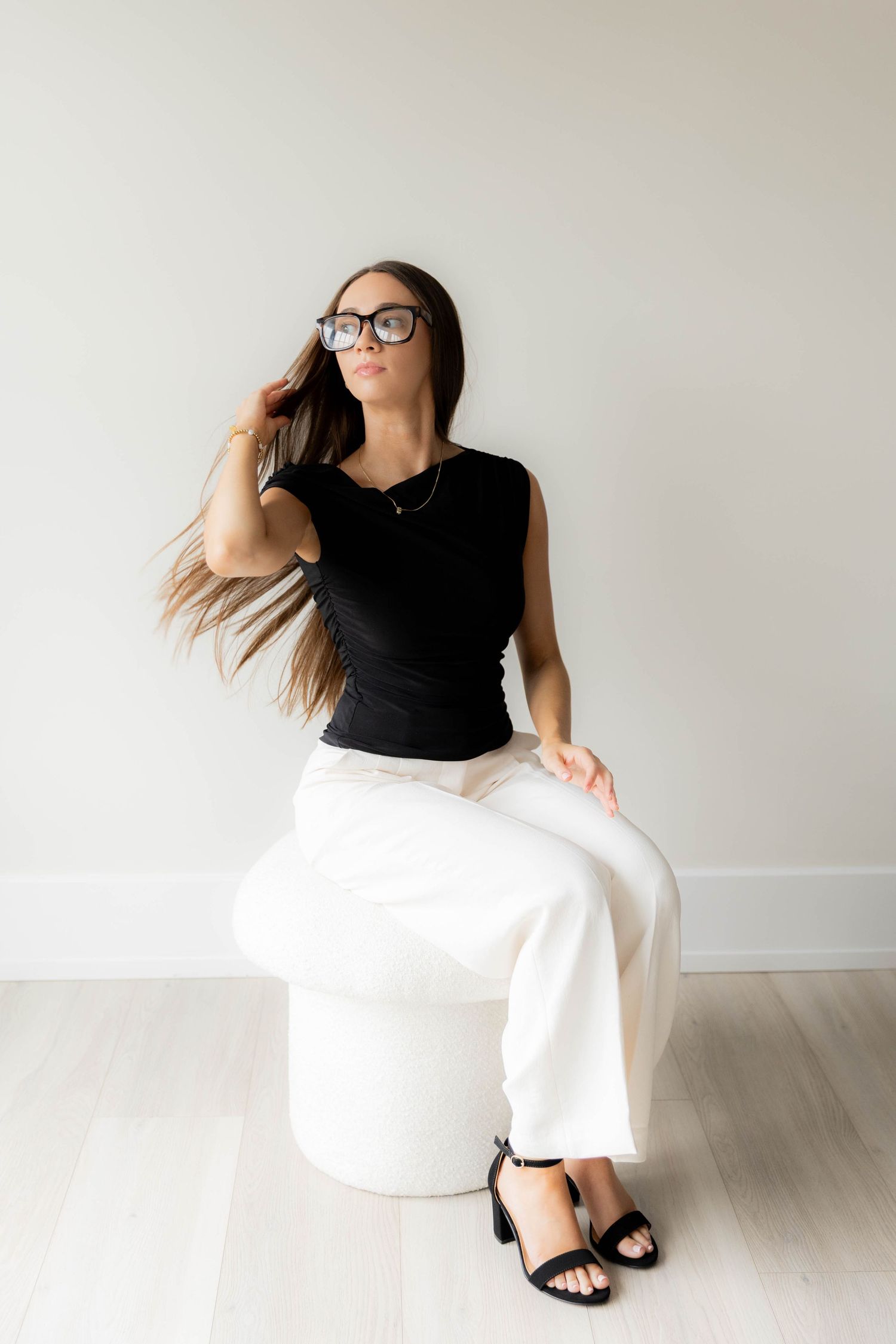Person in black top and white pants seated on white ottoman in bright modern space.