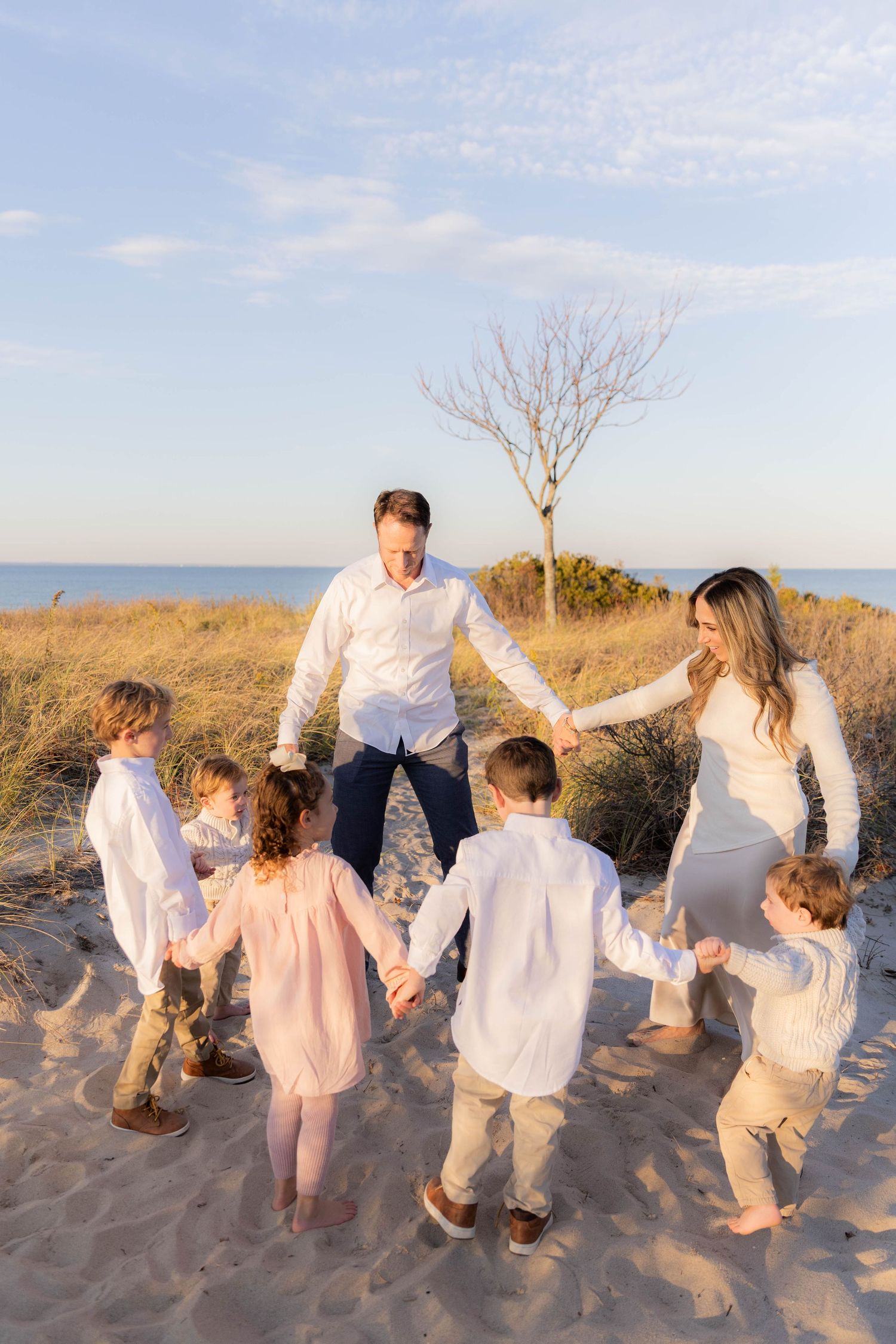 Family in coordinated white outfits playing together on beach during golden hour.