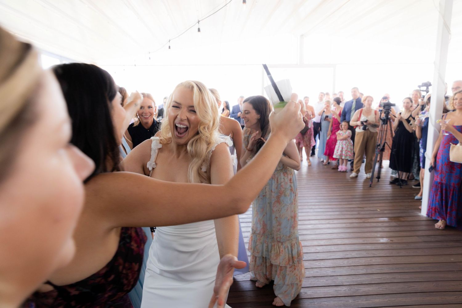 A group of people dancing and celebrating together on a wooden deck at an outdoor party.