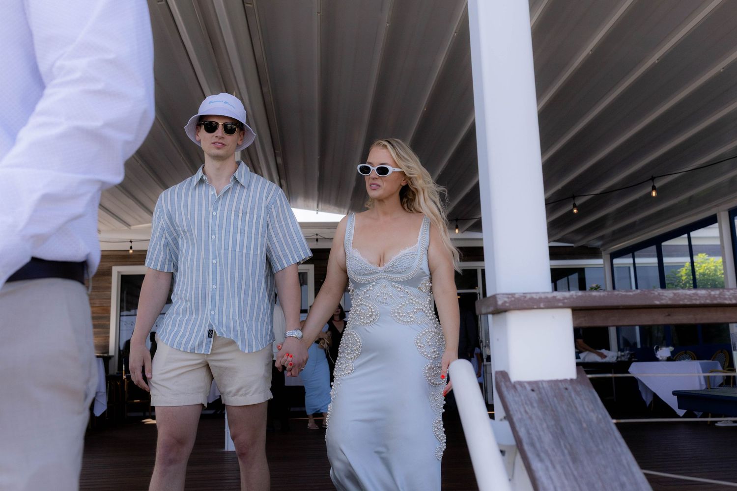 A couple in summer attire holding hands while walking through a covered outdoor area.