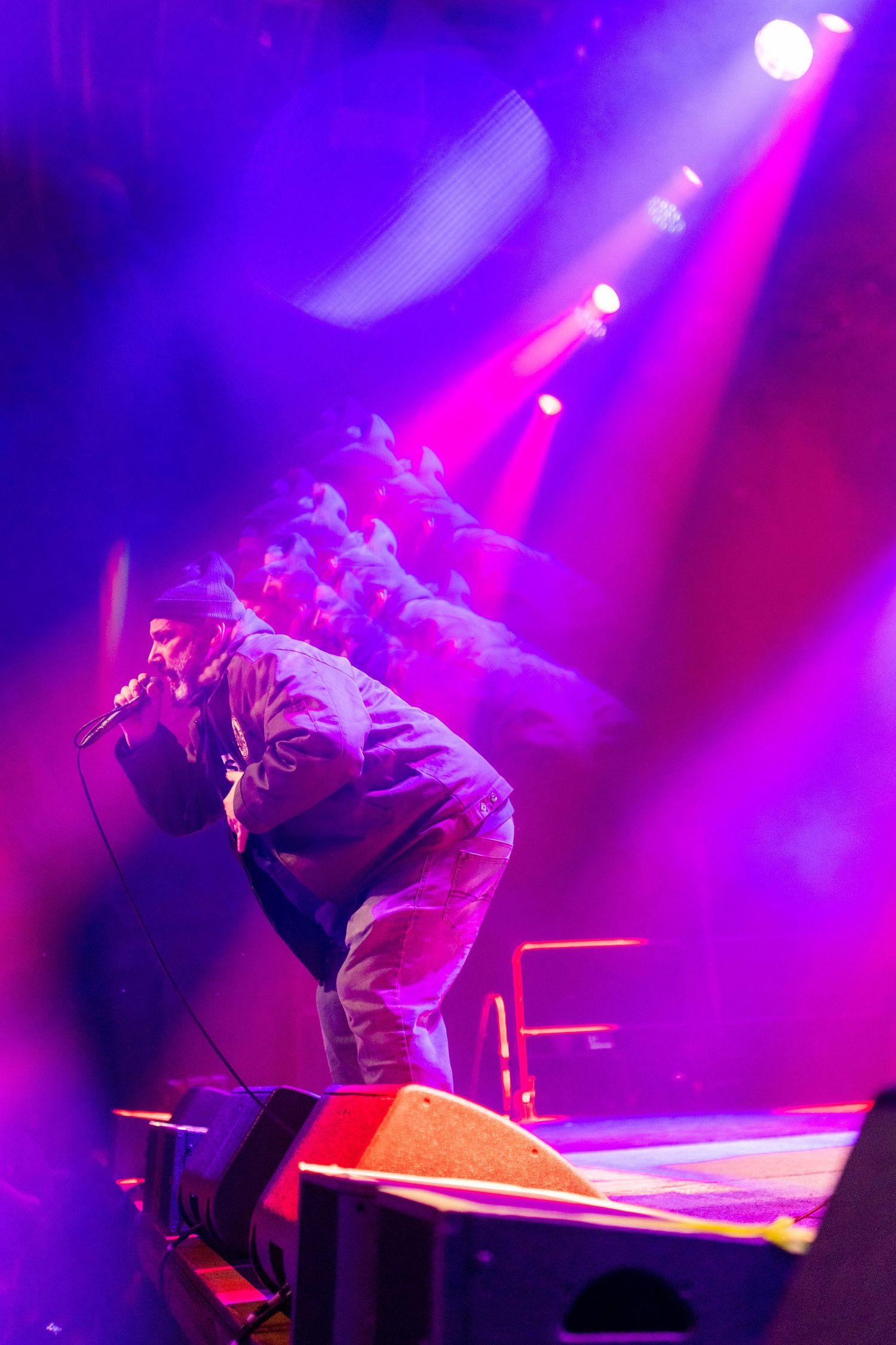 Performer bending over illuminated platform under intense purple and pink stage lighting.
