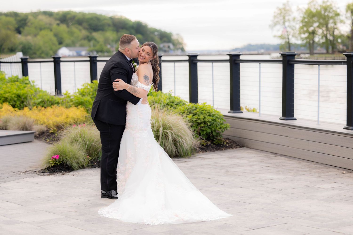 Wedding couple embraces on an outdoor terrace overlooking a waterfront view.
