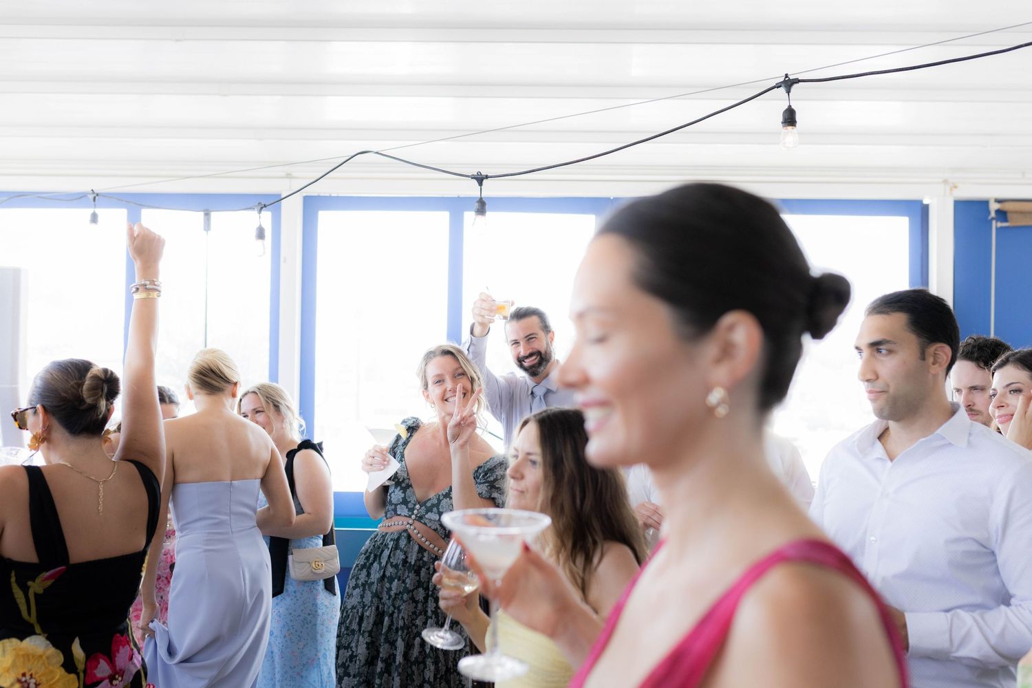 Blurred view of people dancing and mingling at an indoor celebration event with natural lighting.