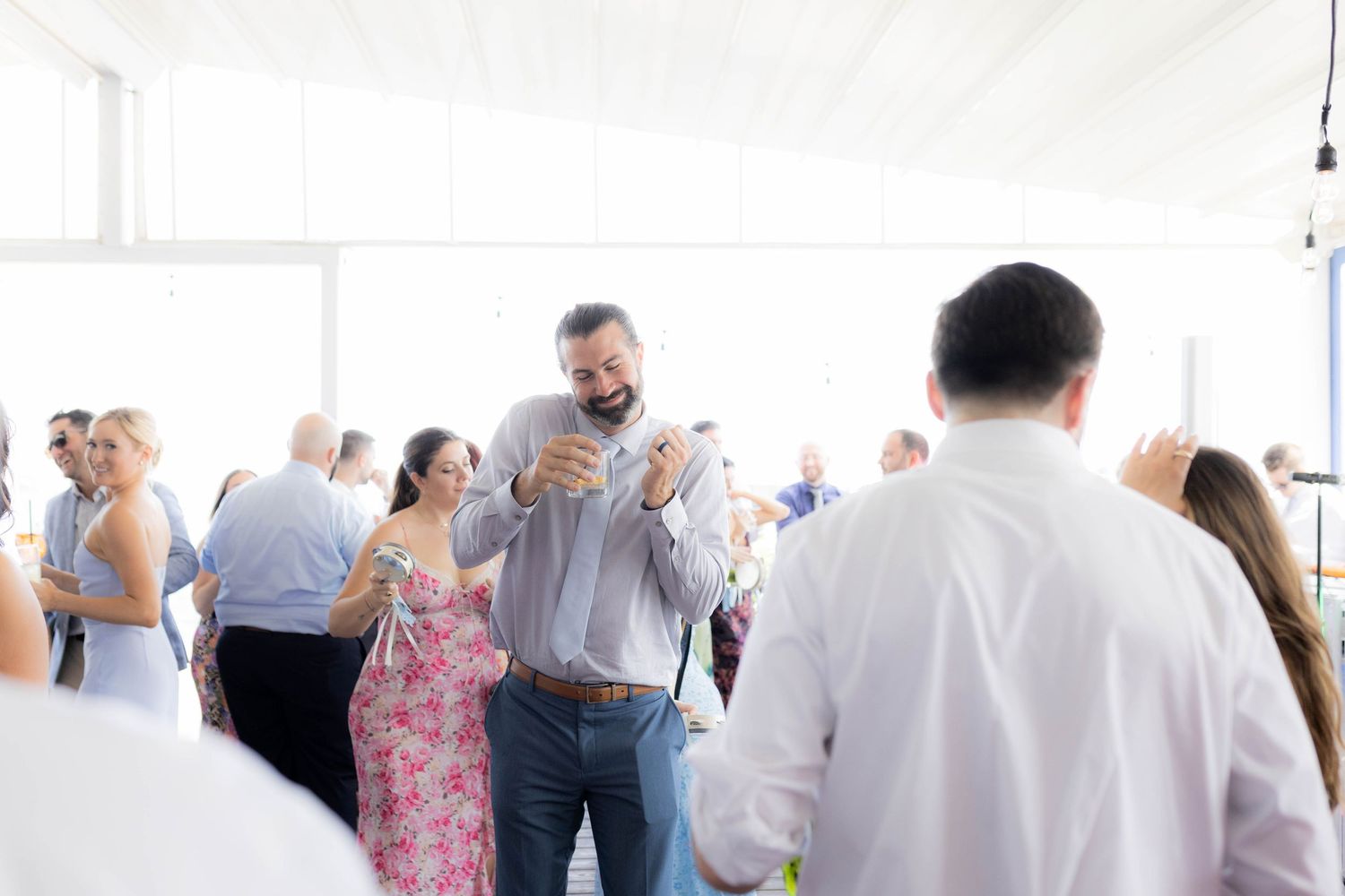 Soft focus crowd of party guests socializing at a bright indoor venue with white walls.