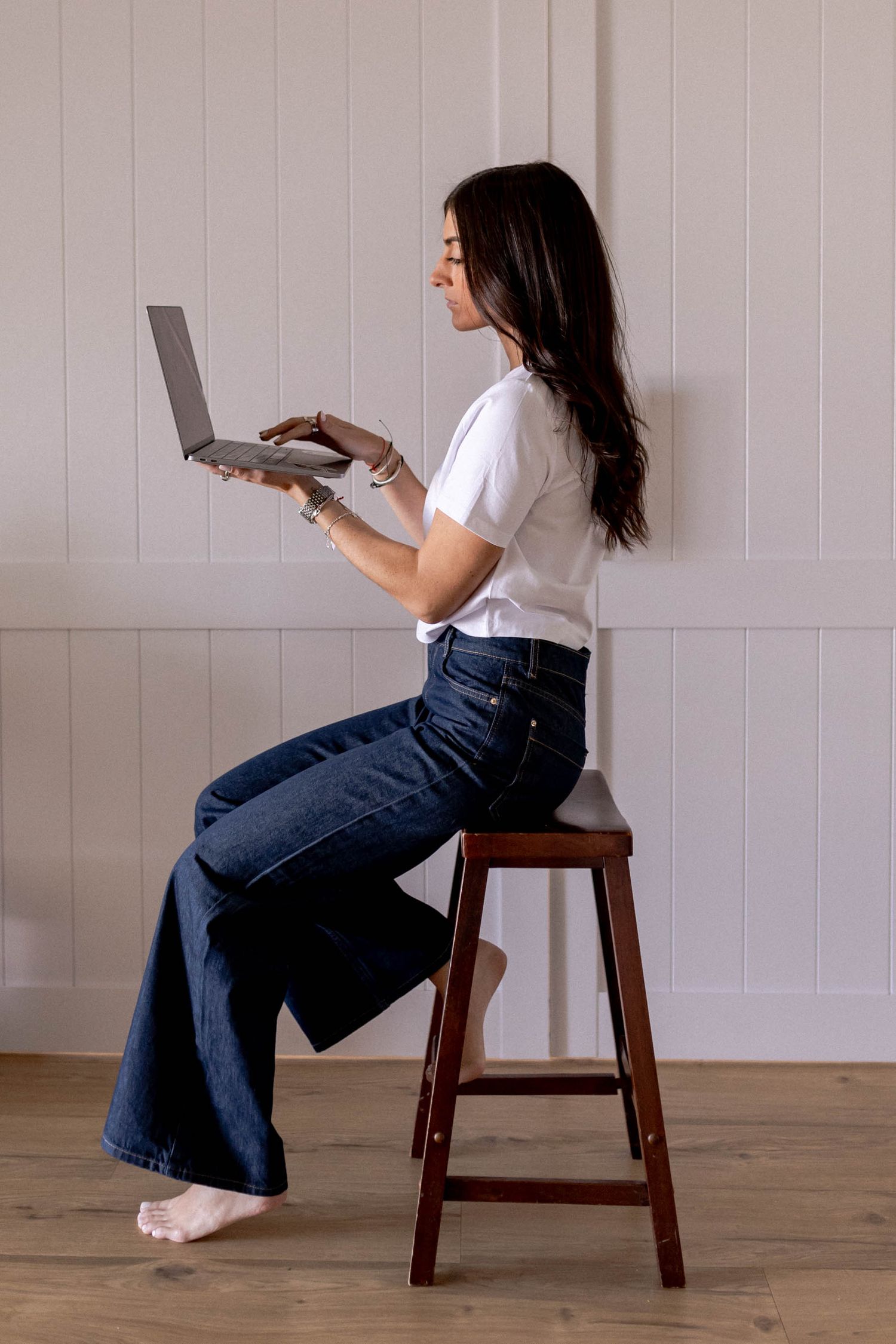 Sequence showing interaction with laptop while seated on wooden stool against white wall.