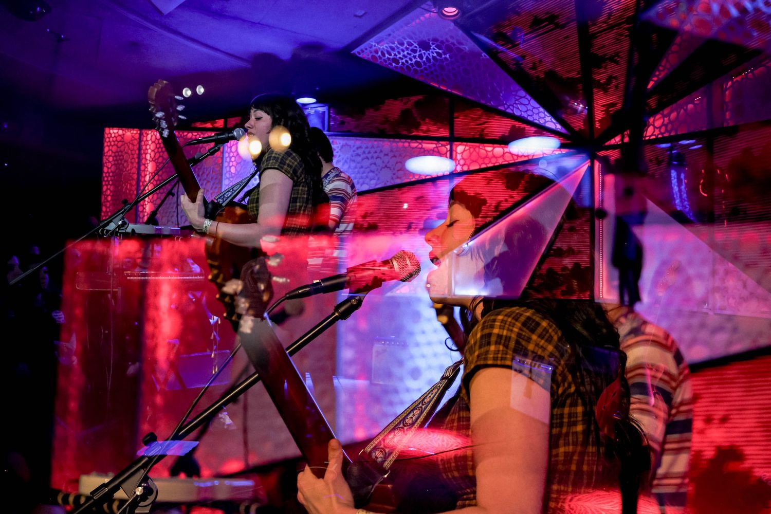 Musicians playing instruments under dramatic purple and red stage lighting.