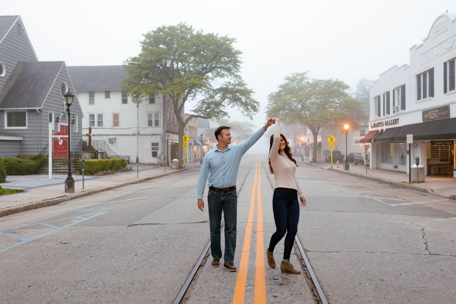 A couple dances together in the middle of an empty small town street at dusk.