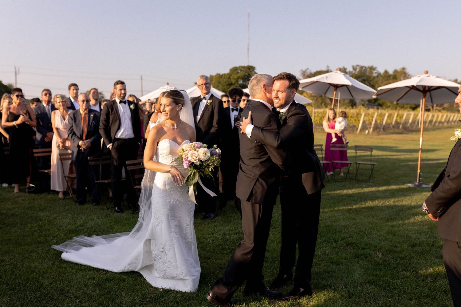 Wedding party members walk across a grassy golf course during golden hour at sunset.