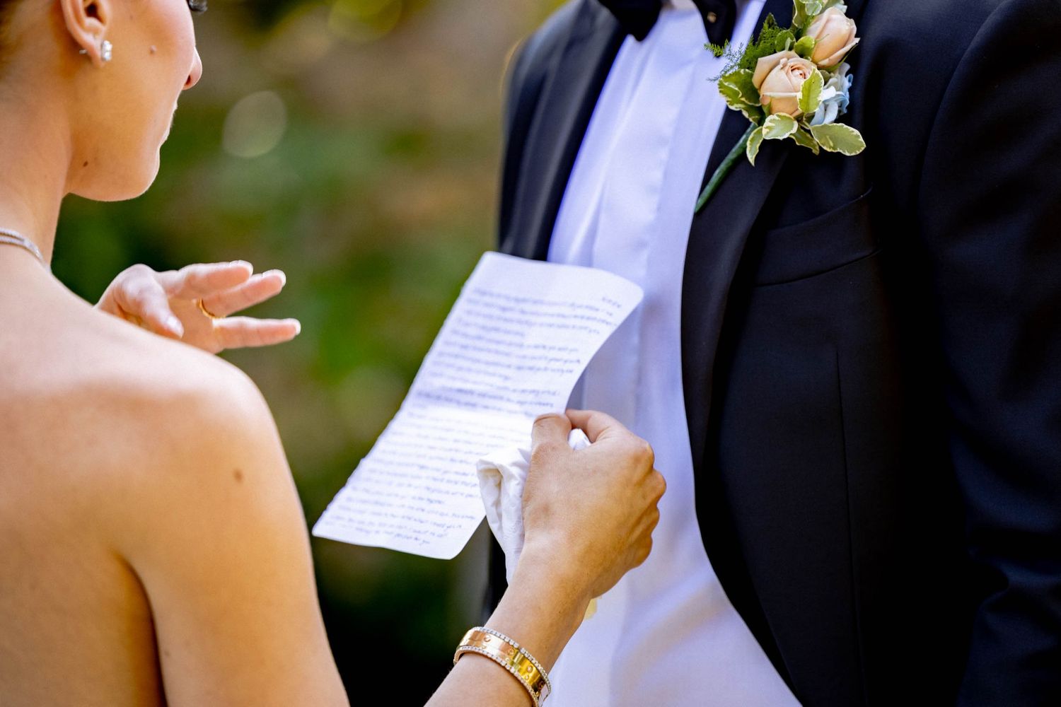 A couple exchanges wedding vows during an outdoor ceremony while holding papers and reading their personal messages.
