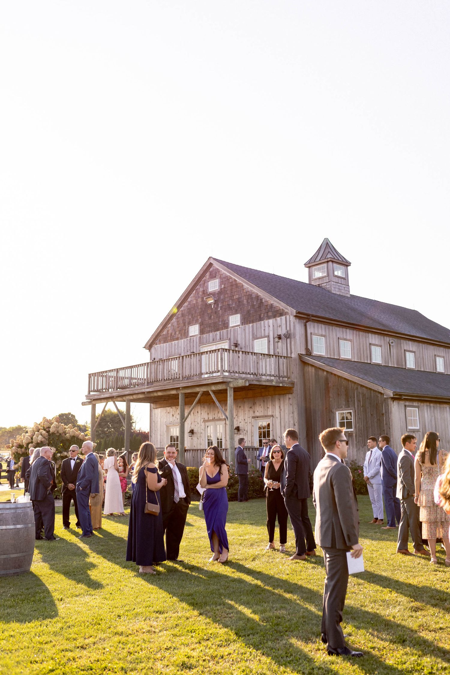 Wedding guests gather outside a rustic barn venue during golden hour at sunset.