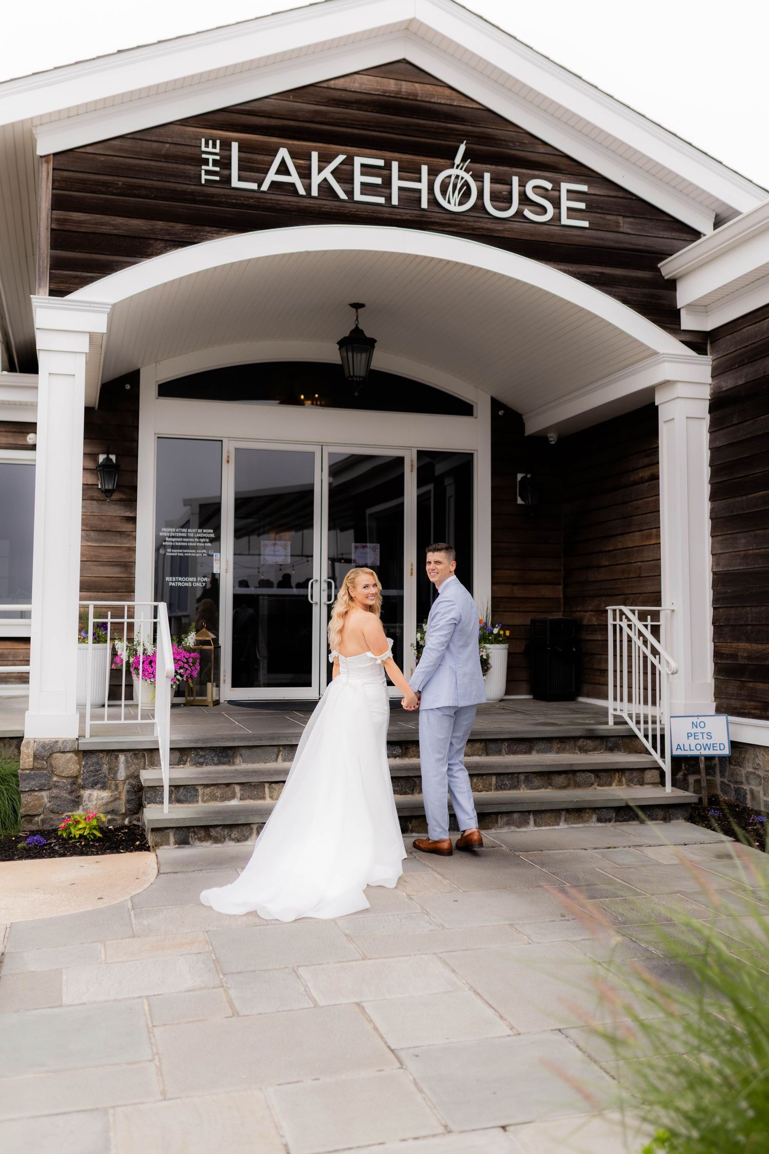 A wedding couple enters The Lakehouse venue through a white columned entrance with rustic wood siding.