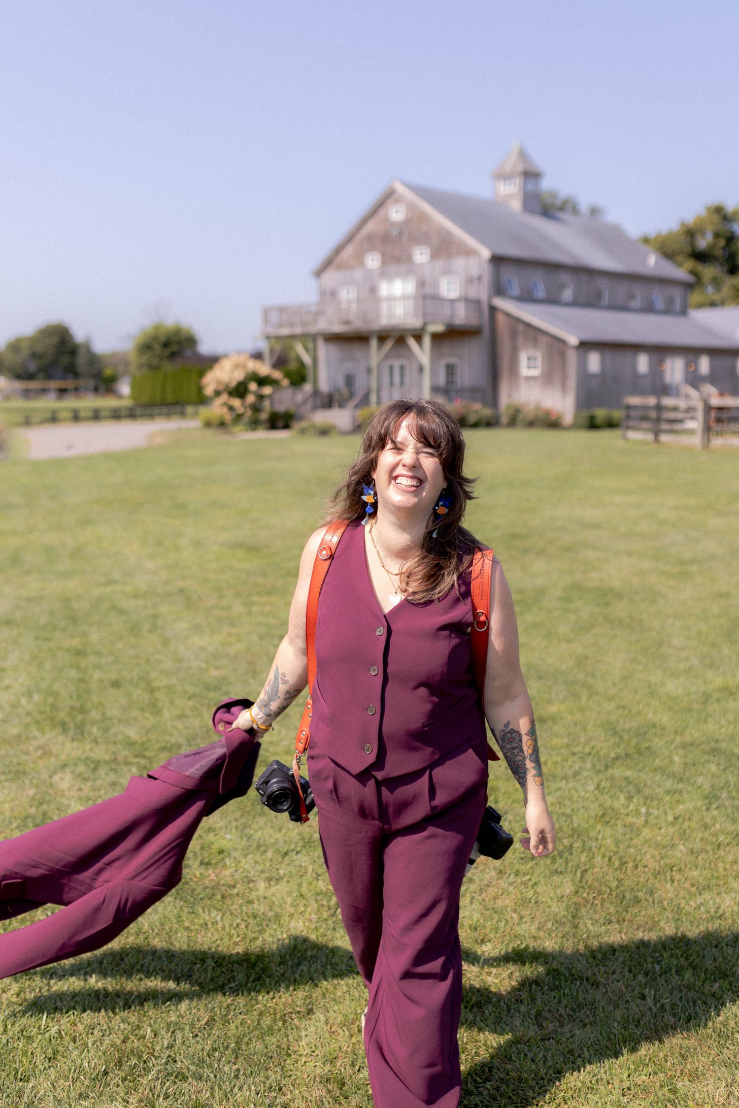 A person in a burgundy dress spins joyfully in a grassy field with a building visible in the background.