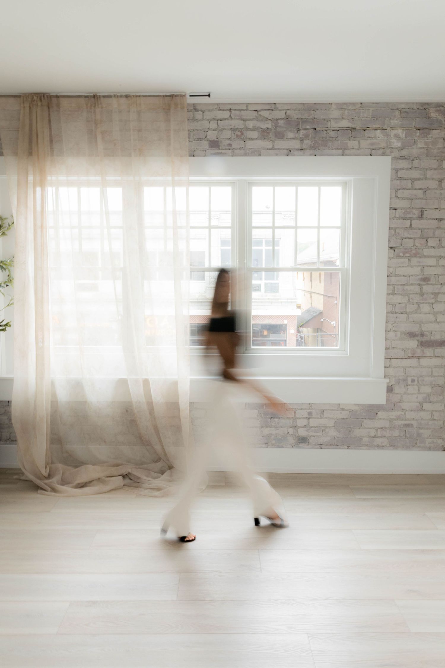 Motion blur photograph of person walking through bright white minimalist room with brick walls.