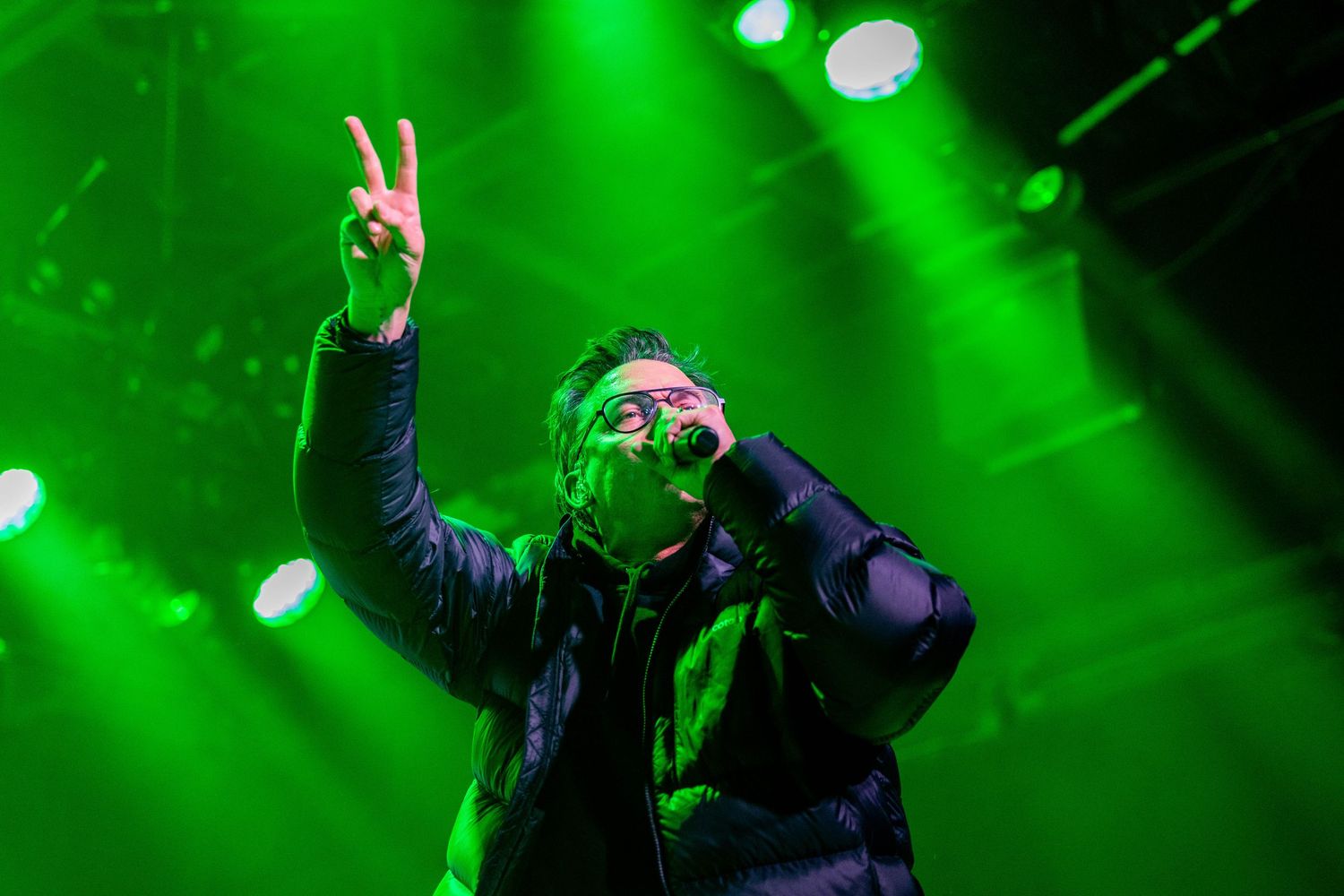 Live performance captured under bright green stage lights with dynamic movement.