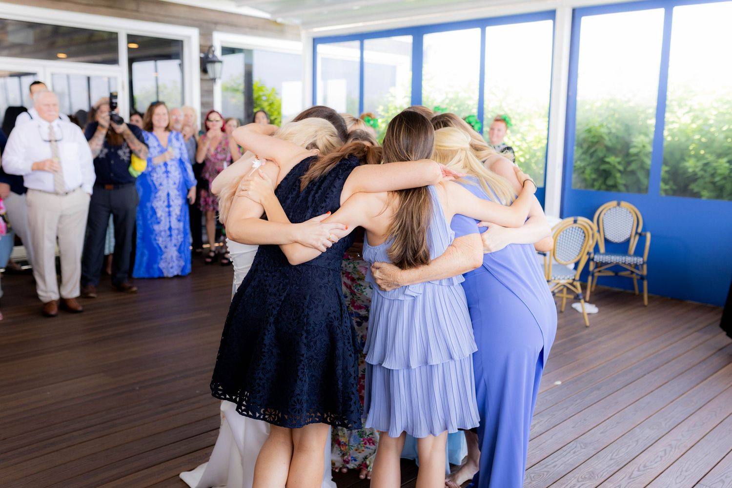 Wedding guests embracing in a circle during a celebration in an elegant venue with panoramic windows.