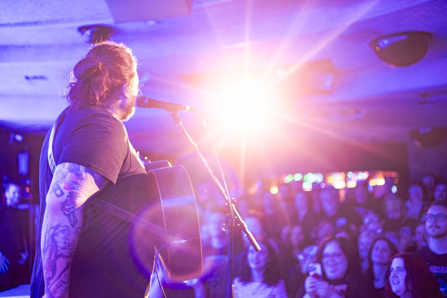 Concert crowd silhouetted against bright purple stage lighting during live performance.