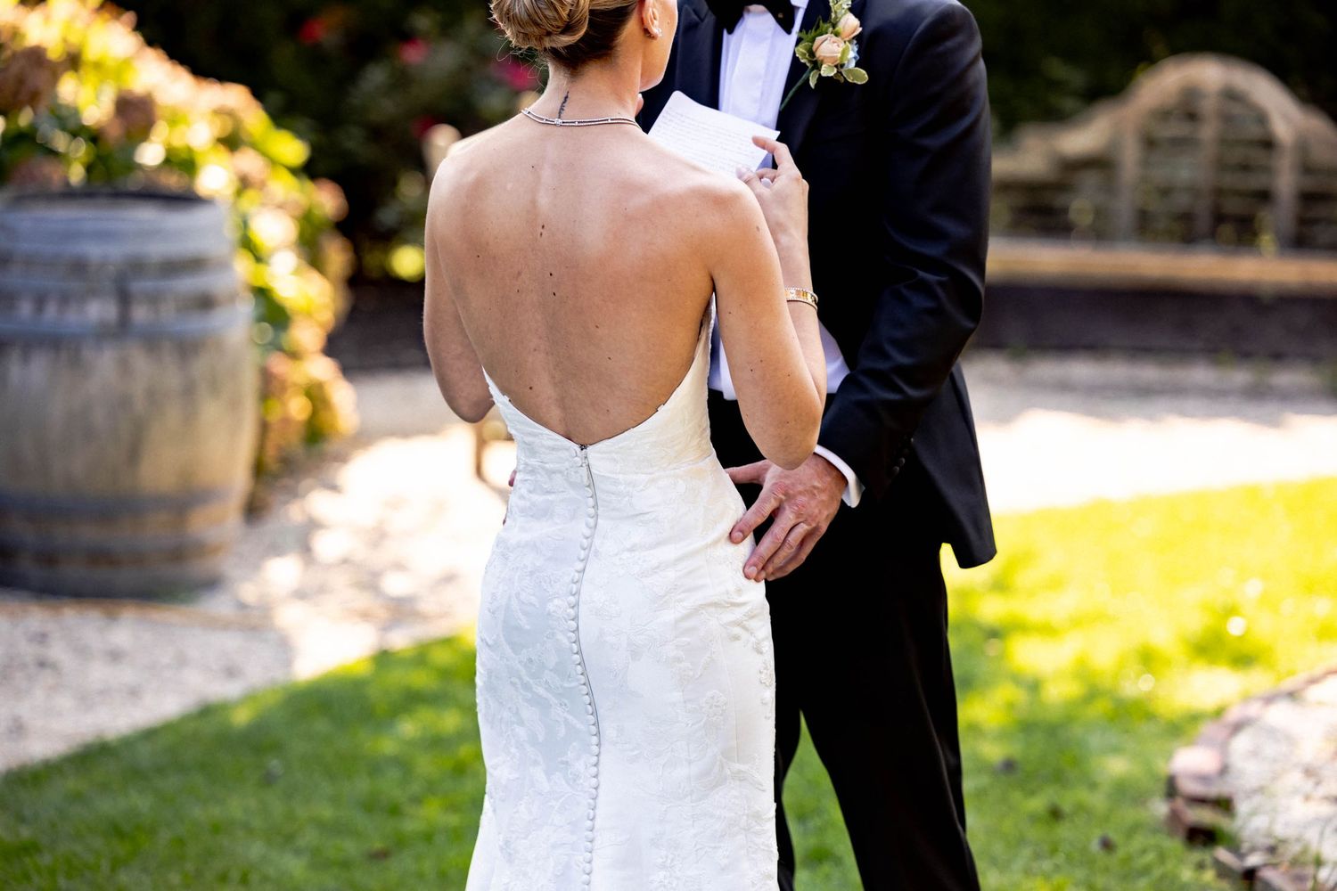 A couple in wedding attire embraces on a lush green lawn during their outdoor celebration.