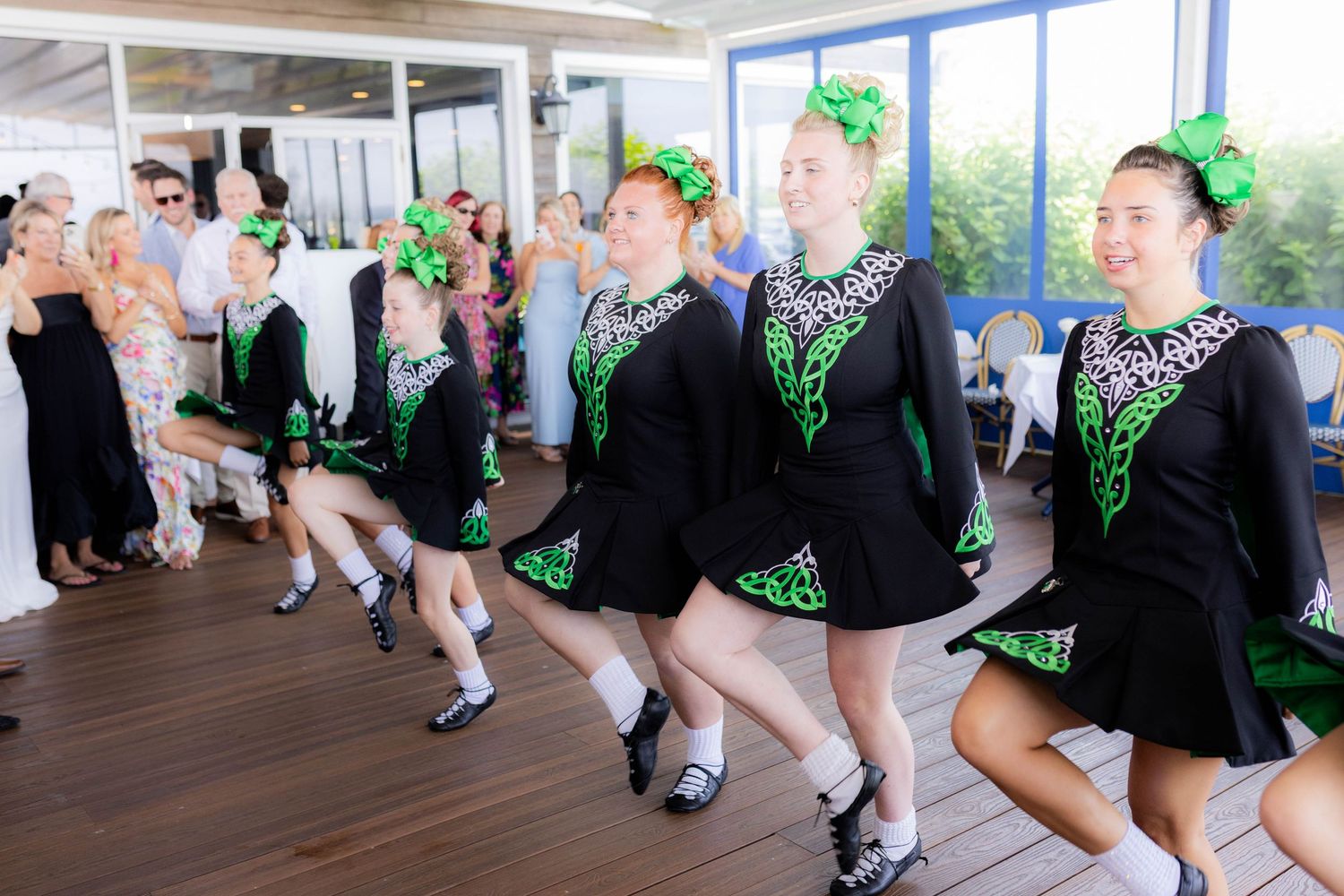 Dancers in black and green costumes perform synchronized leg kicks during a dance routine.