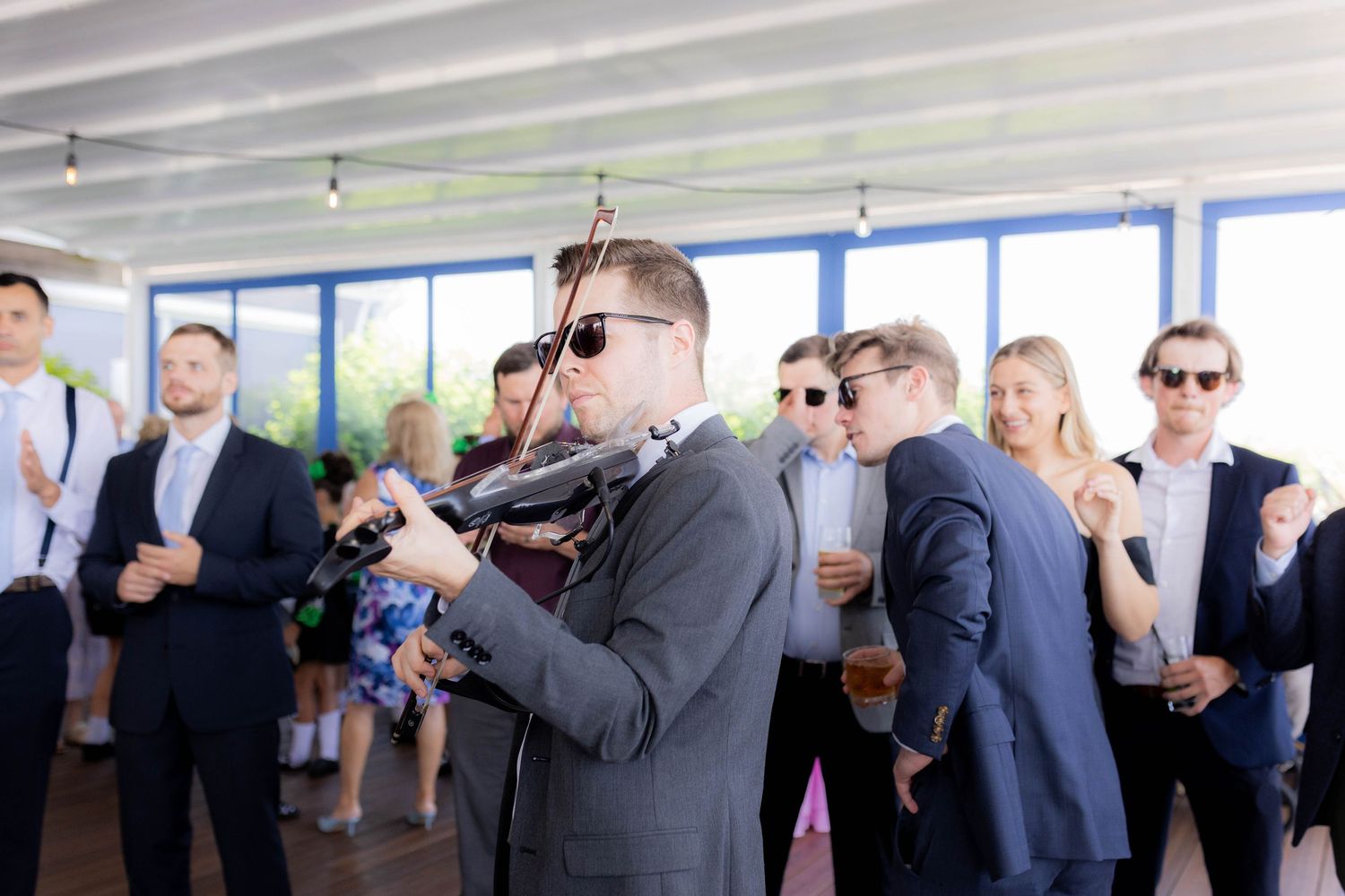 Wedding party guests dance and celebrate together on a wooden deck during an outdoor reception.
