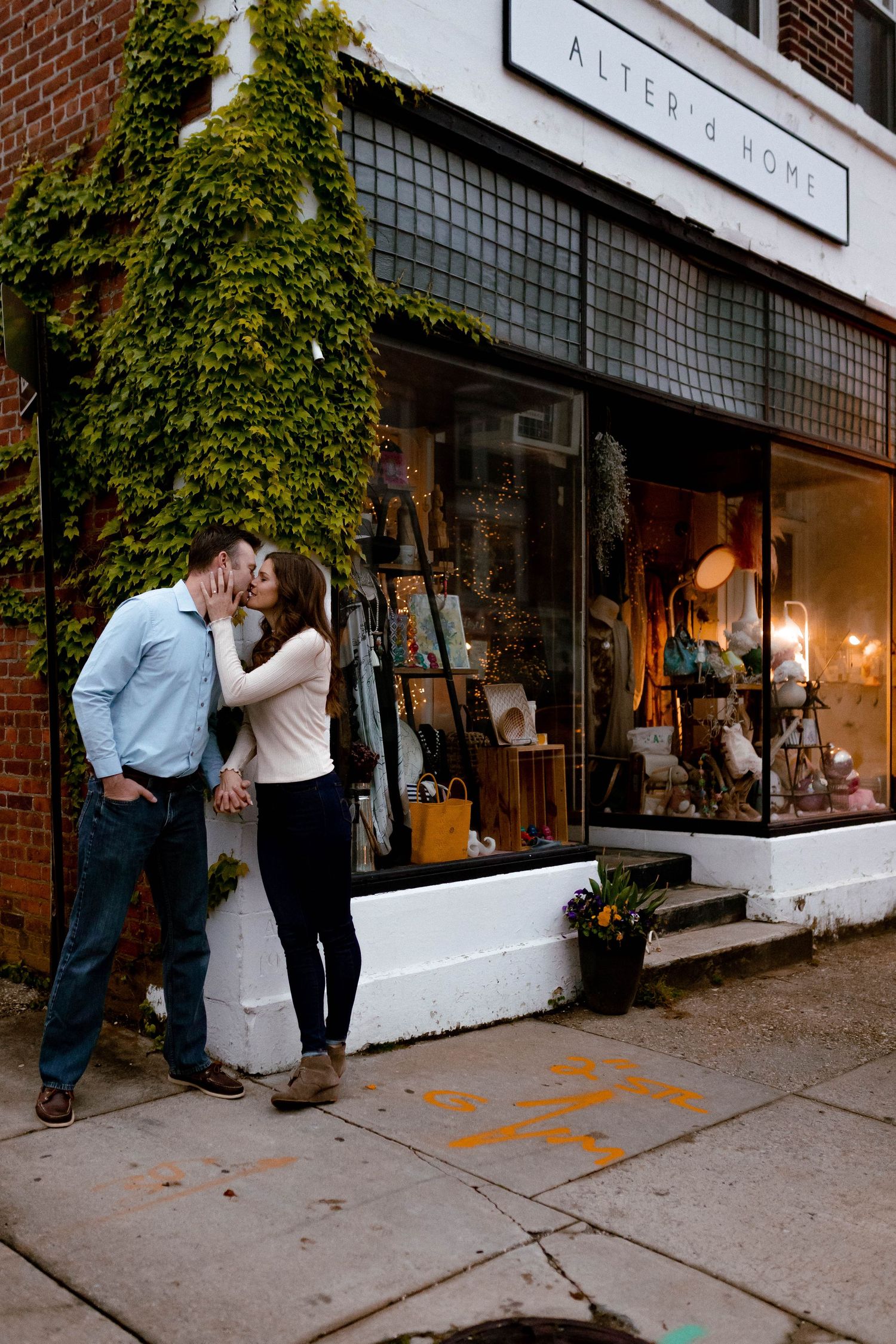 Couple stands outside a brick storefront with large display windows and ivy-covered walls.