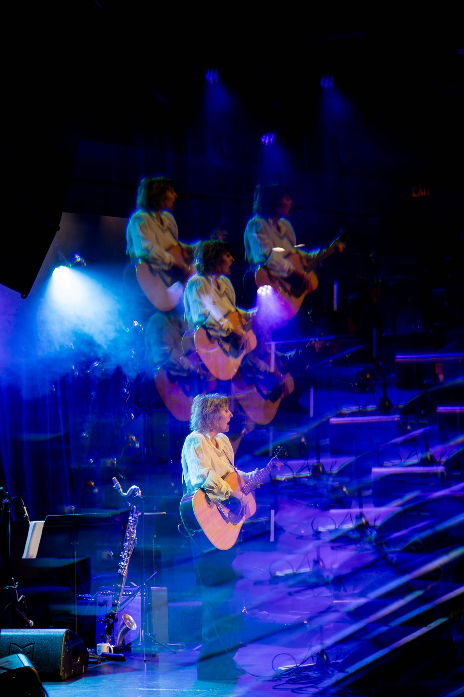 Multiple exposure shot creates dreamy effect of musician playing acoustic guitar in blue stage lighting.