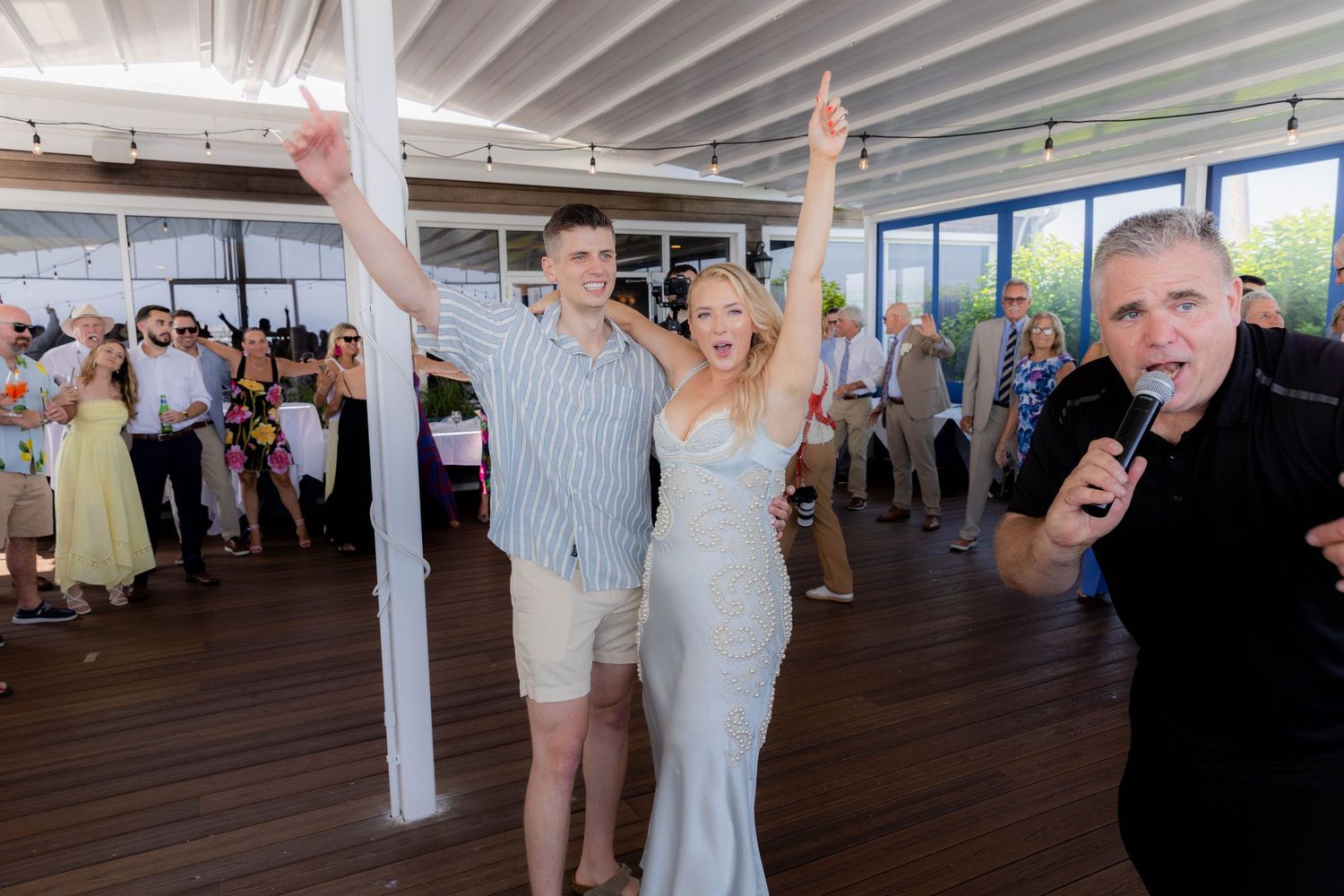 Wedding guests dance and celebrate together on a covered outdoor patio during a reception party.
