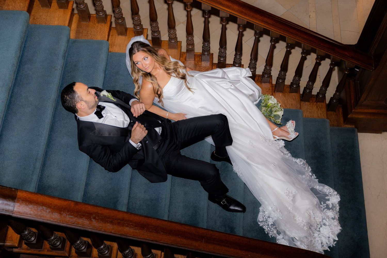 A couple performs a dramatic dance dip pose on a wooden staircase during what appears to be a wedding celebration.