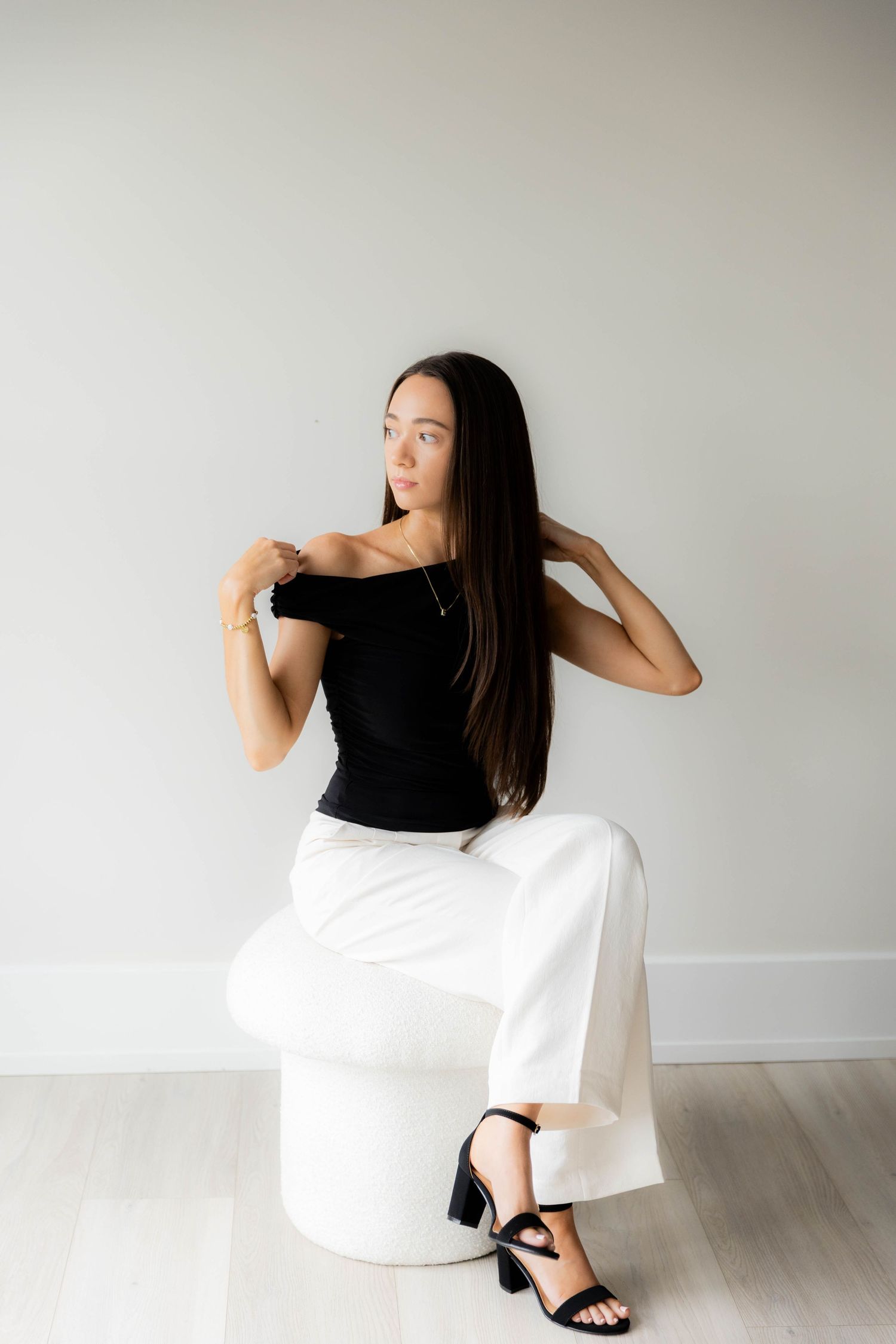 Dynamic pose of person in black top and white pants against neutral wall background.