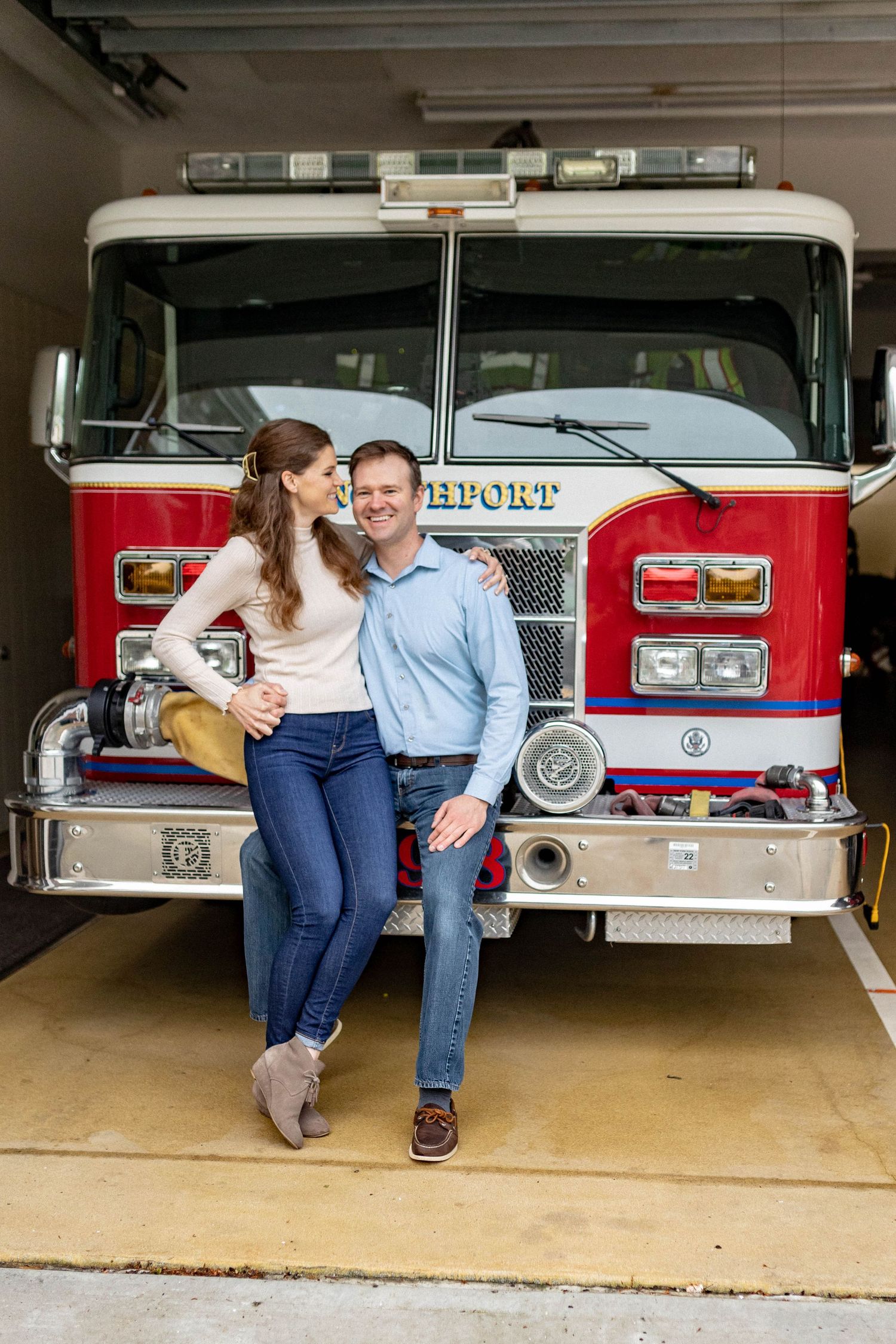 A couple sits together in front of a row of vintage fire trucks in a fire station garage.