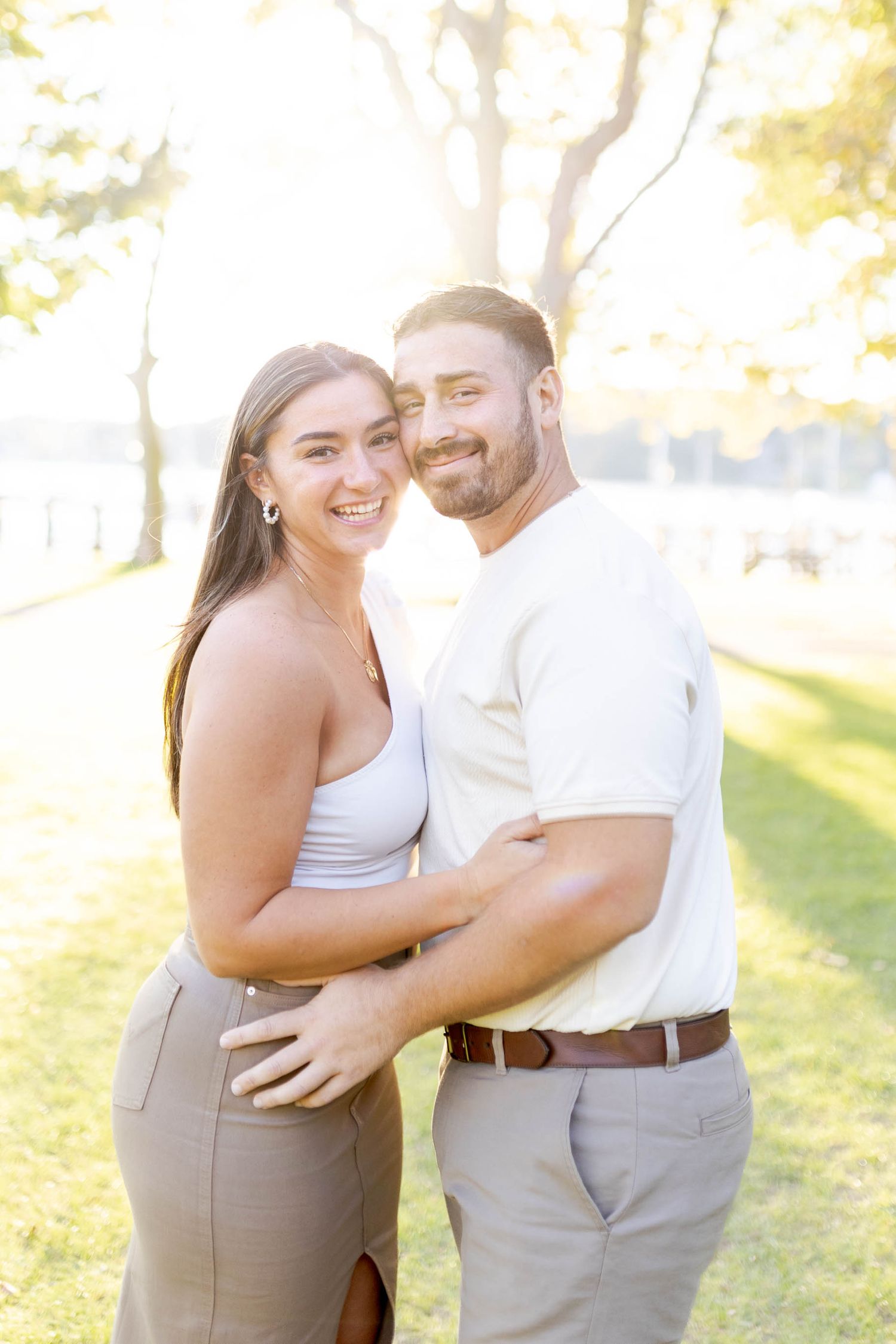 A couple shares intimate moments in a sun-drenched park setting wearing coordinated white and beige outfits.