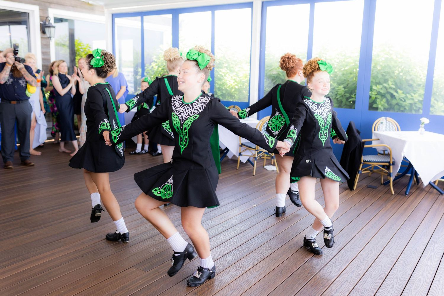 Irish dancers performing traditional dance moves in black and green costumes on a wooden floor.
