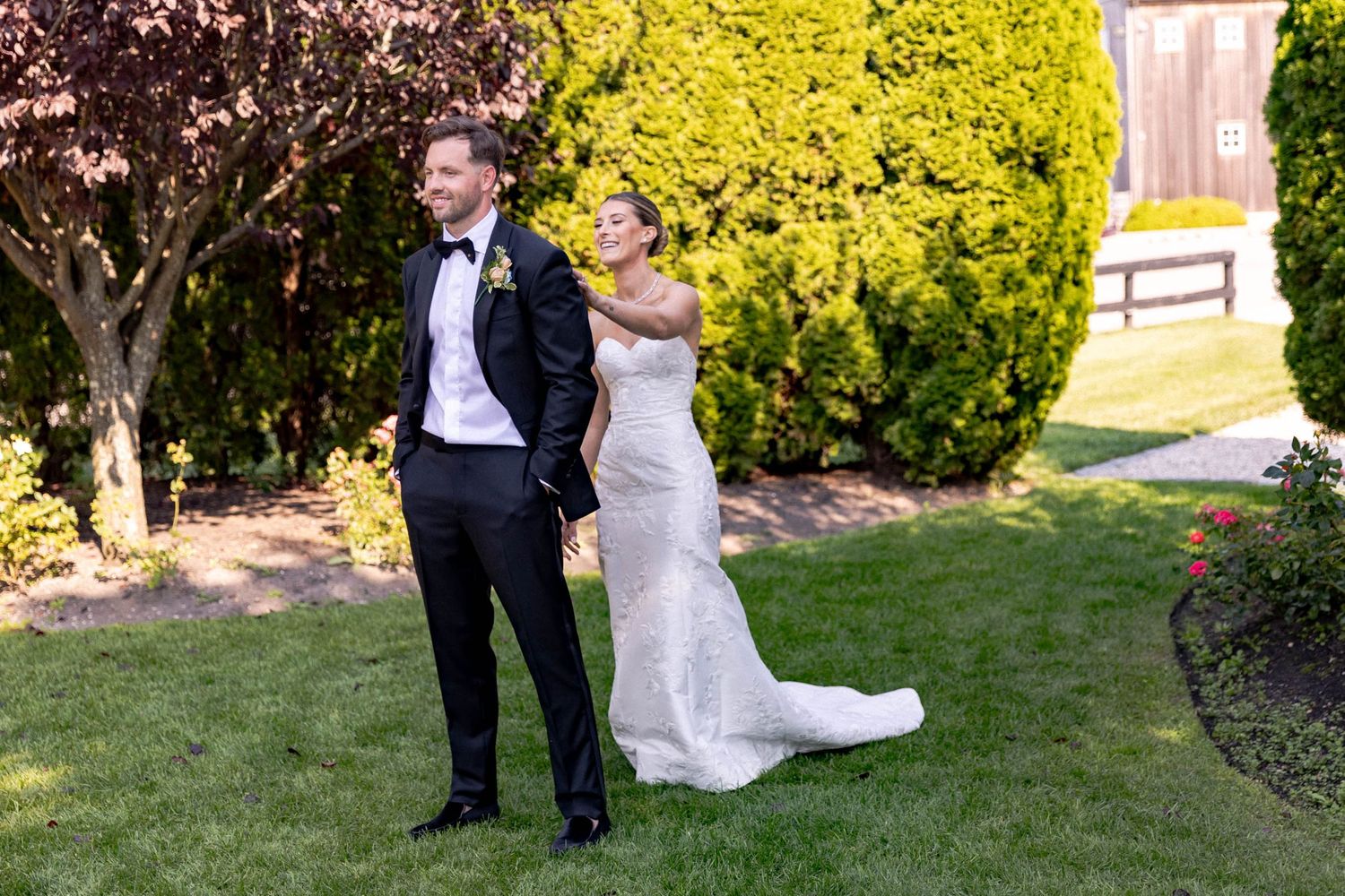 A couple in formal wedding attire shares a playful moment while walking through a garden setting.