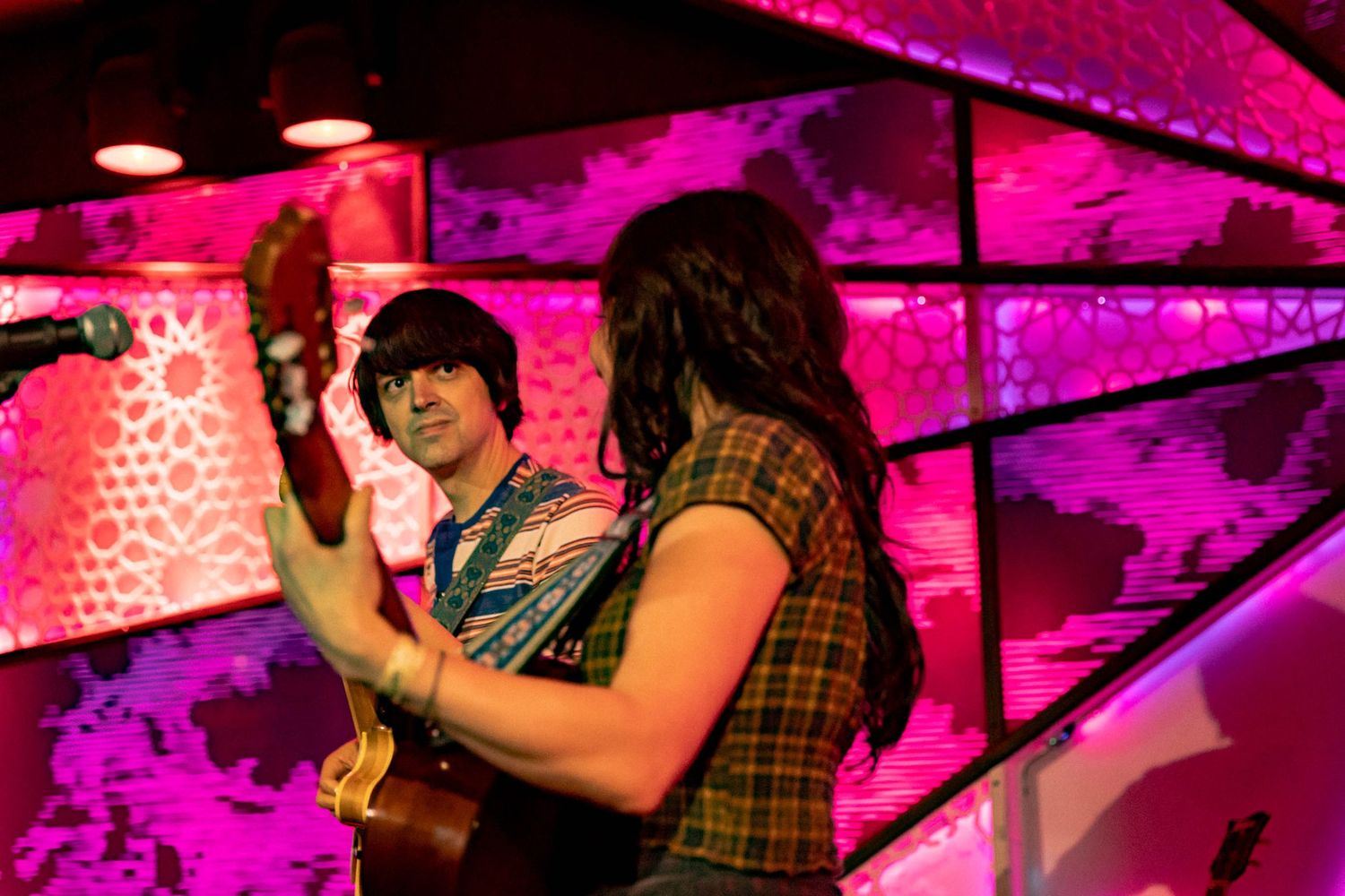 Musicians playing instruments under bright magenta stage lights at live concert venue.