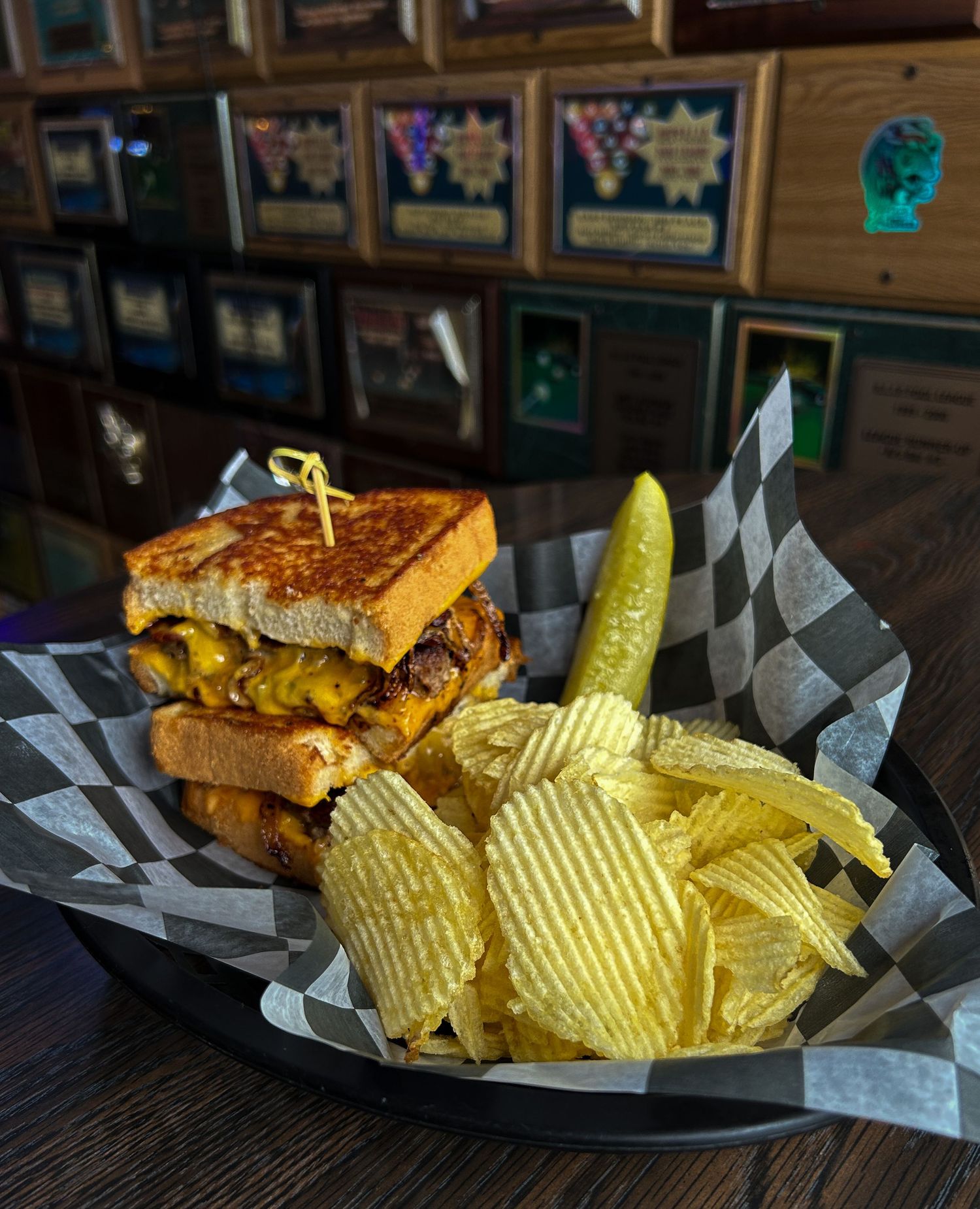 Grilled patty melt sandwich with melted cheese on toasted bread, served with crispy chips and a dill pickle in a basket.