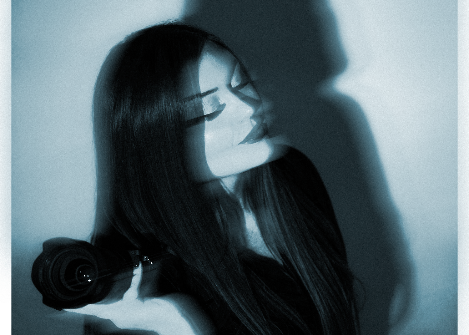 A woman with long dark hair poses gracefully, holding a black rose in a moody blue-toned artistic portrait.