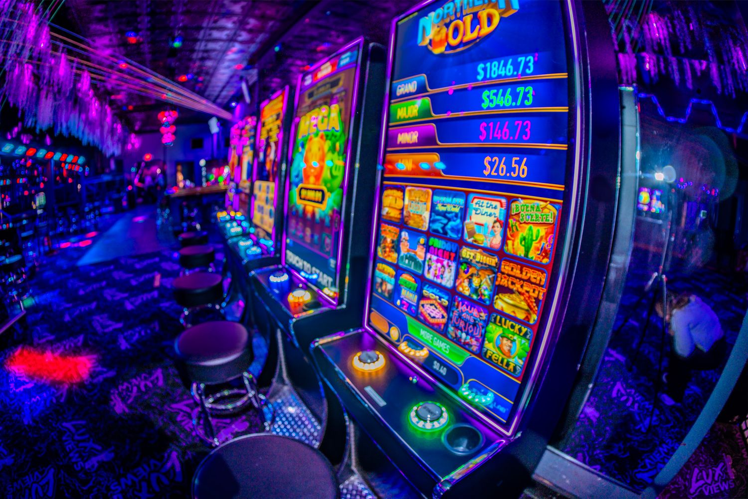 Vibrant neon-lit casino slot machines glowing in purple and blue light with gold jackpot displays on the gaming floor.