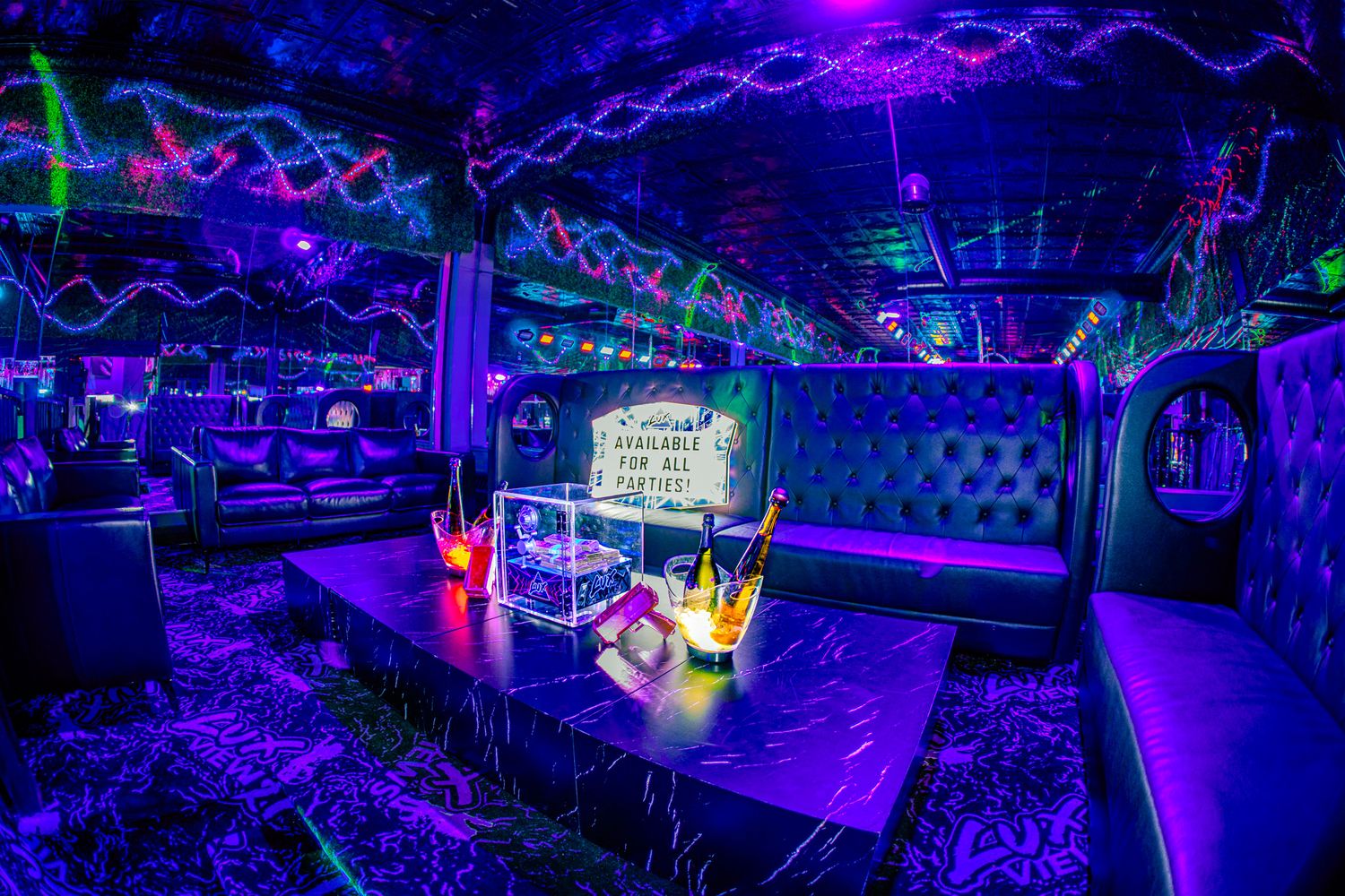 Glowing neon nightclub VIP booth with UV lights, tufted seating, champagne bottles, and vibrant purple ambiance.