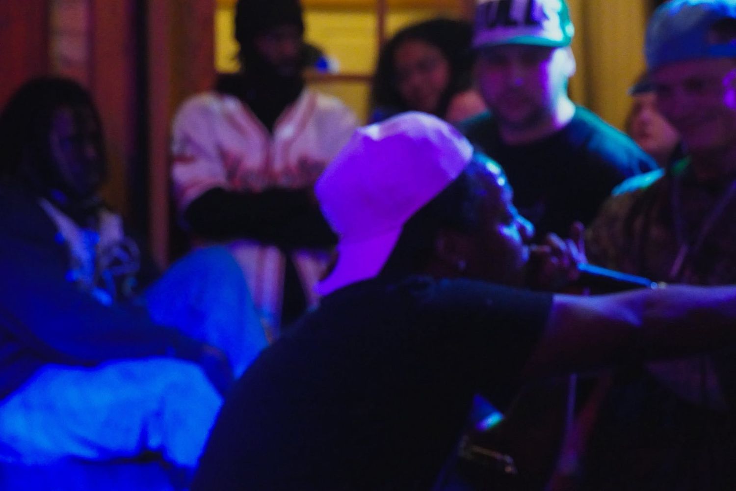 Group of people gathered at a dimly lit venue with blue and purple lighting during a social event.