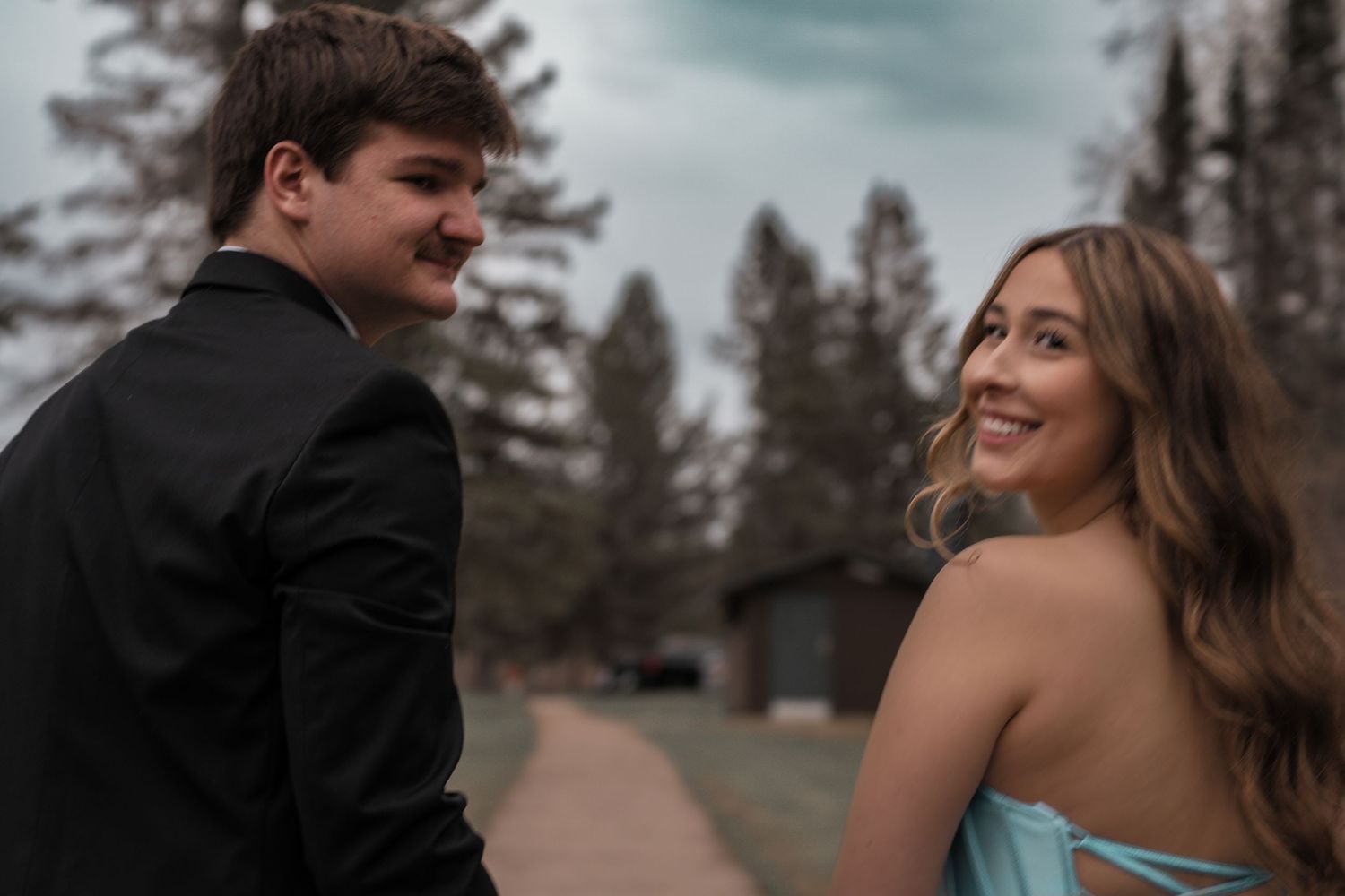 Young couple in formal wear smiling outdoors near trees, dressed for prom or special occasion.