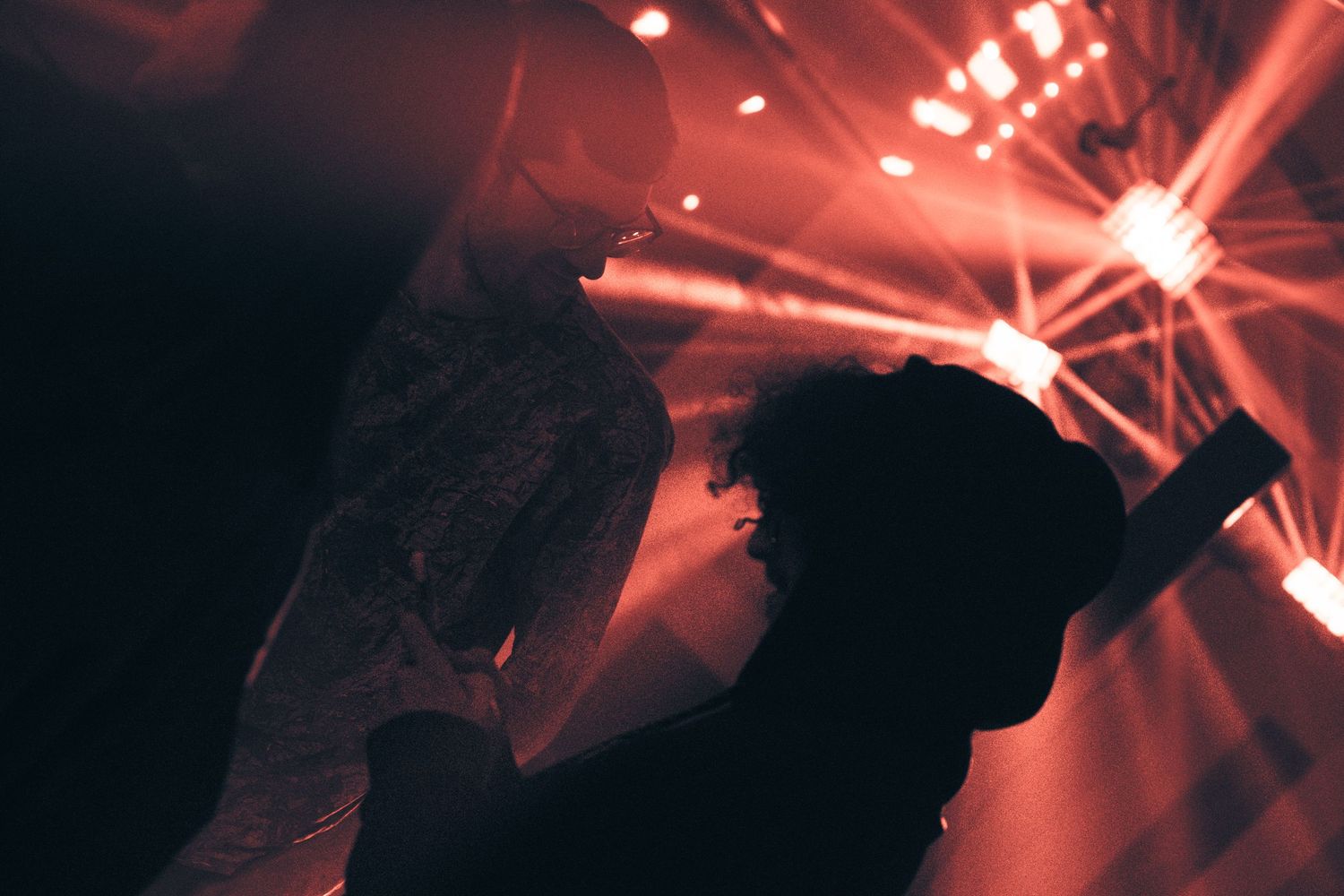 Silhouetted performers on stage with dramatic red and white light beams at a live concert event.