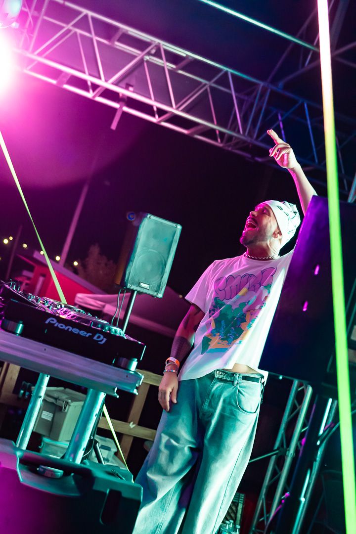 DJ performing at night on stage with Pioneer DJ equipment under vibrant pink and green lights.