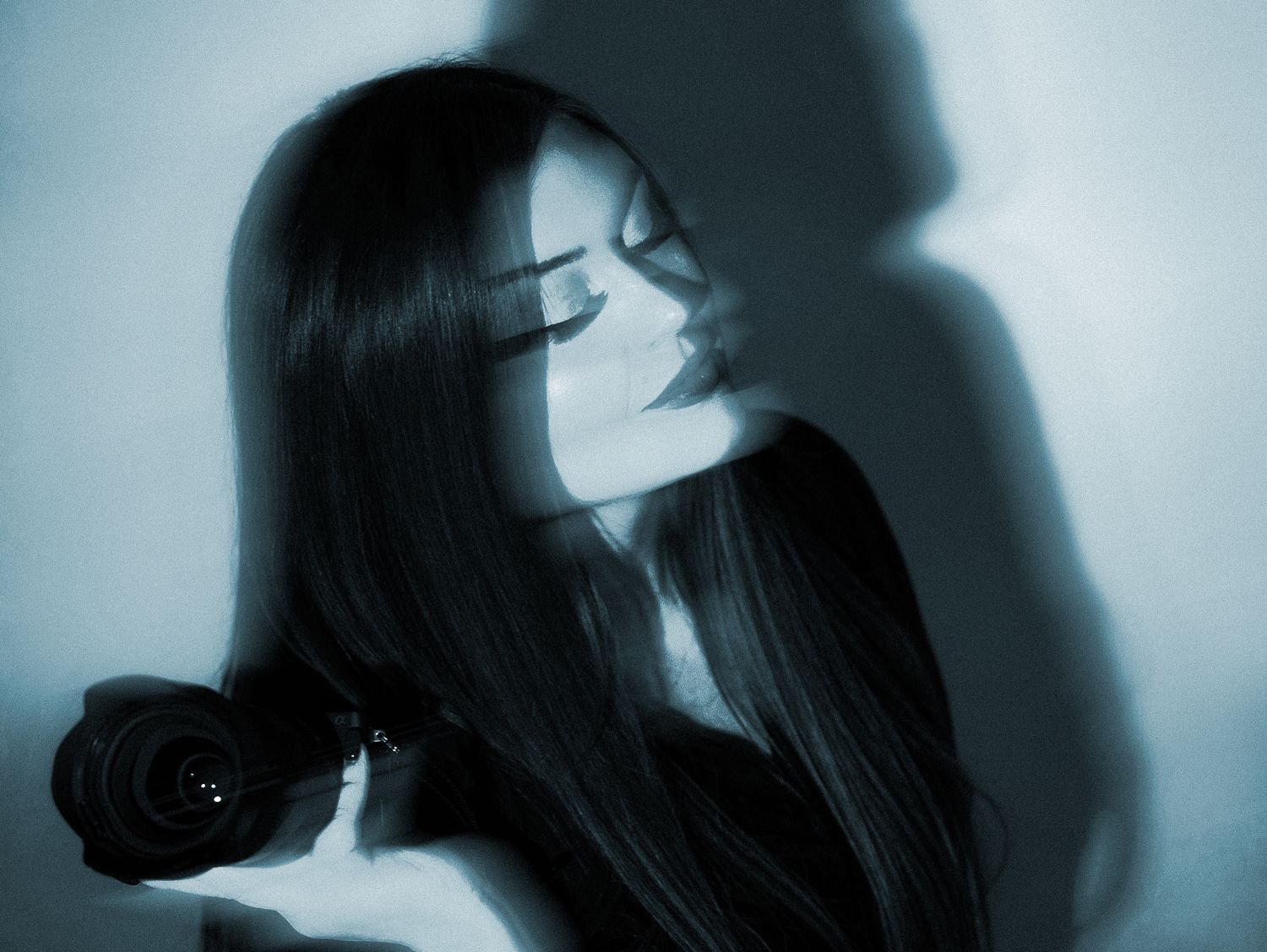 A young woman with long dark hair holds a black rose, bathed in moody blue-toned light with dramatic shadows.