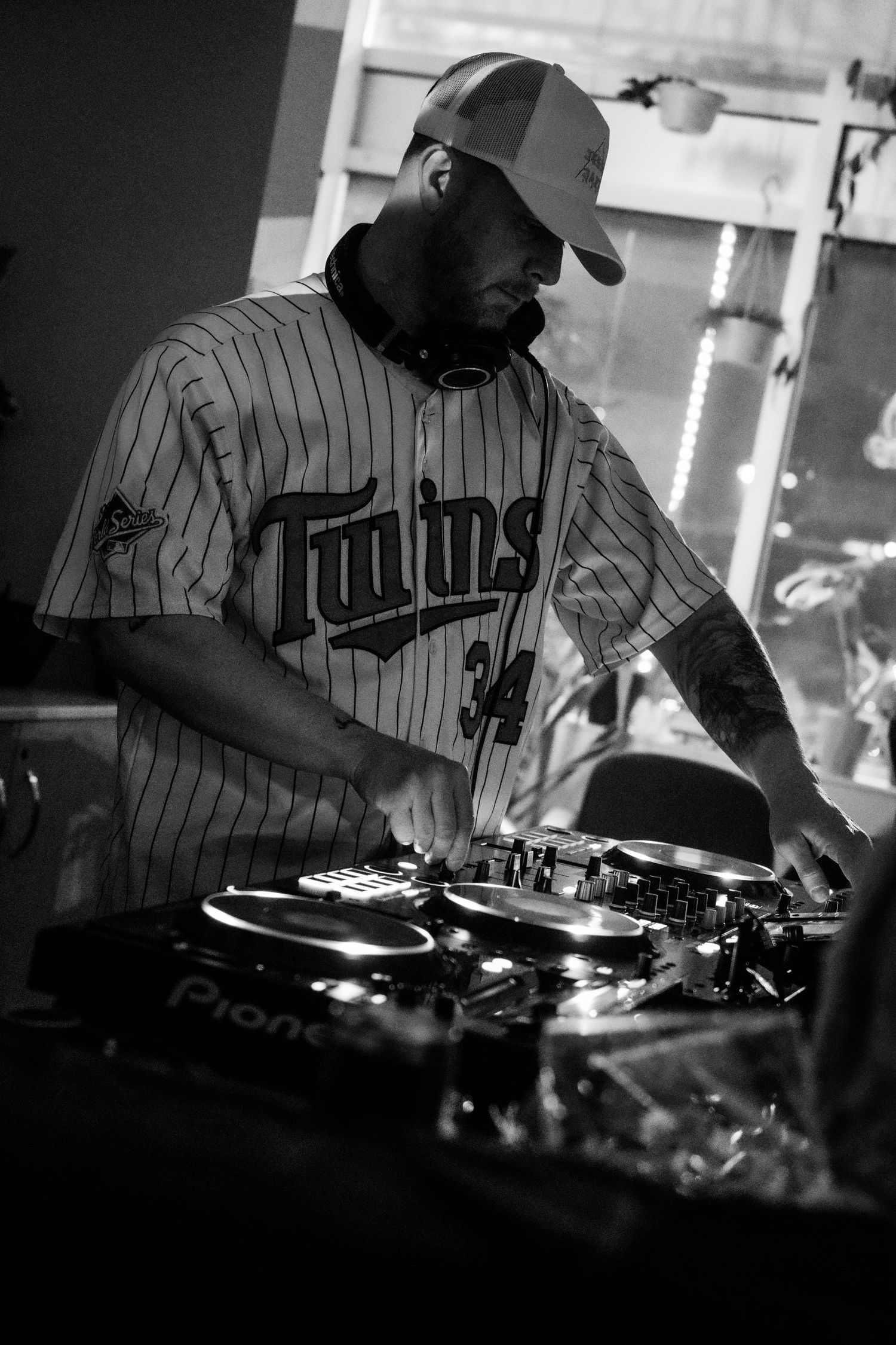 Bearded DJ in Twins baseball jersey working Pioneer turntables in black and white photo.