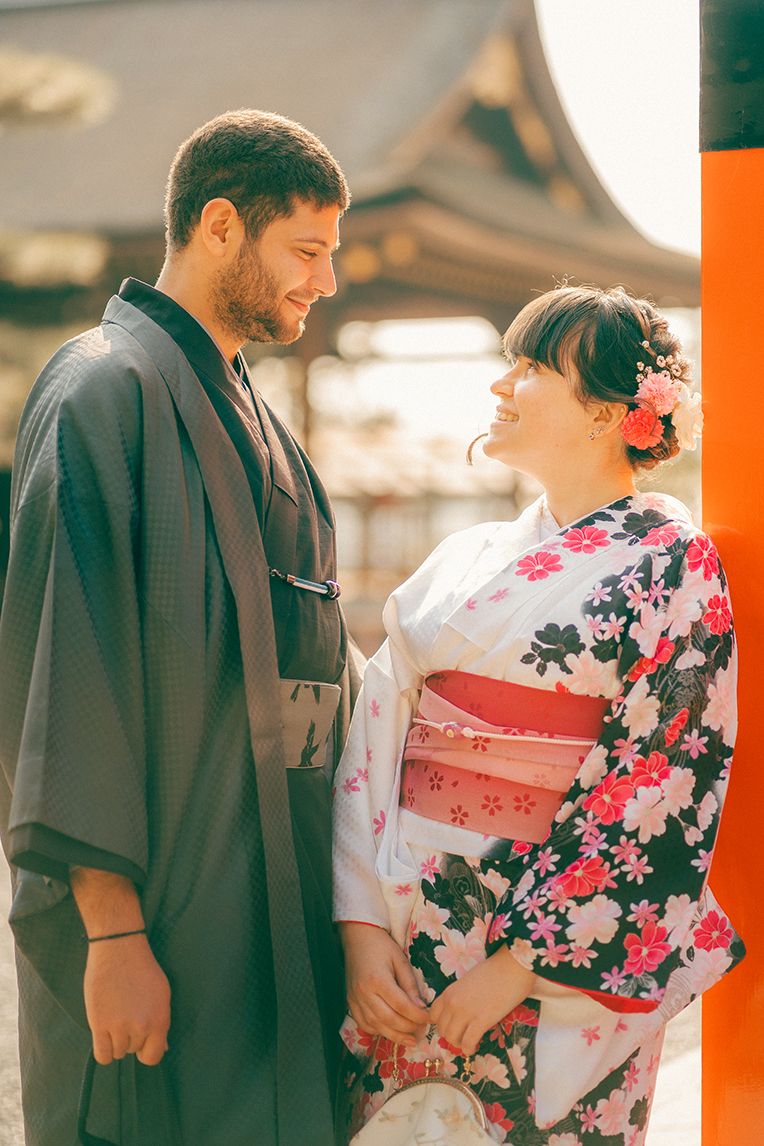 A couple in traditional Japanese attire, with the woman wearing a floral kimono and the man in dark clothing, share a moment.