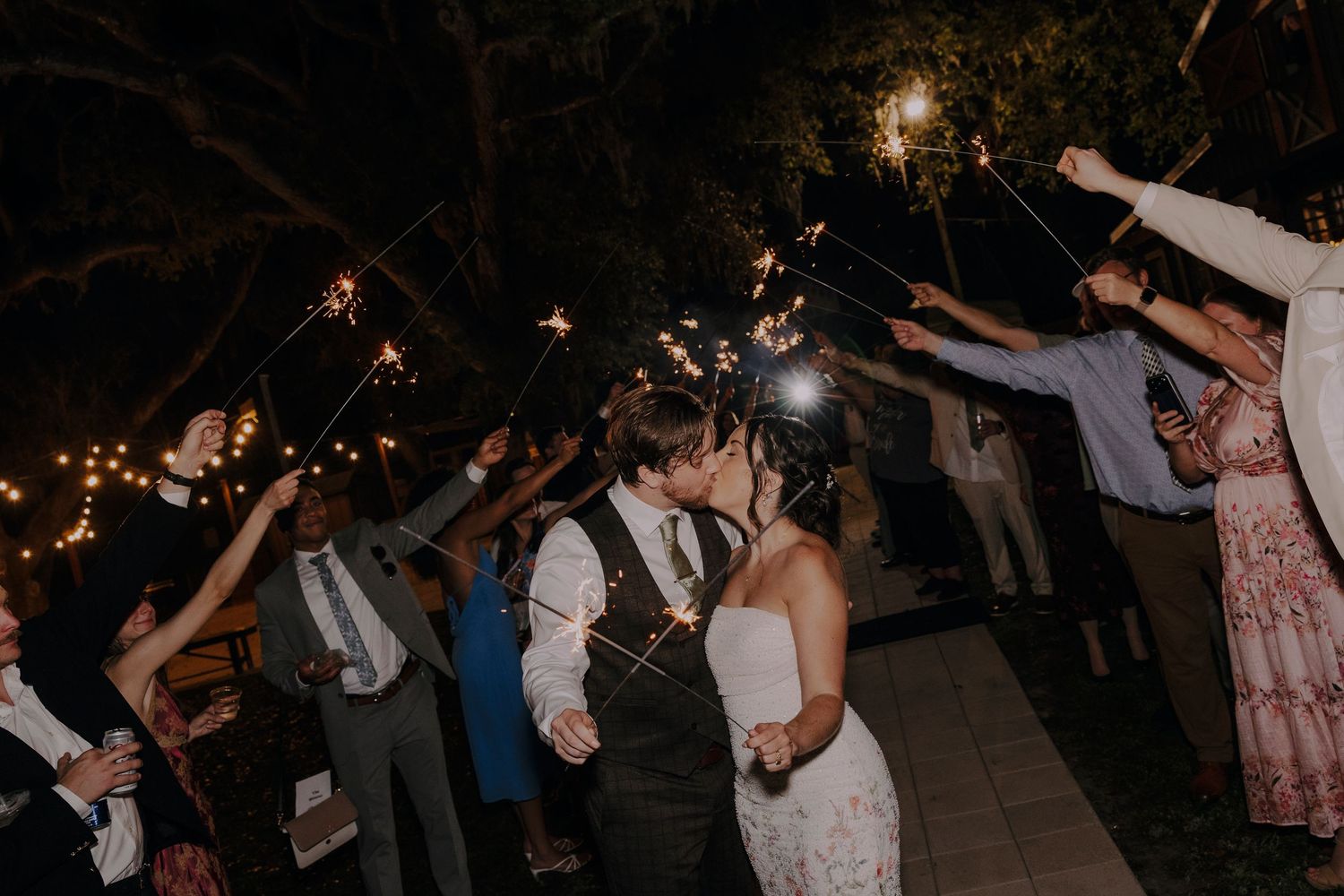 Bride and groom share a kiss during a romantic sparkler send-off at their outdoor evening wedding reception.