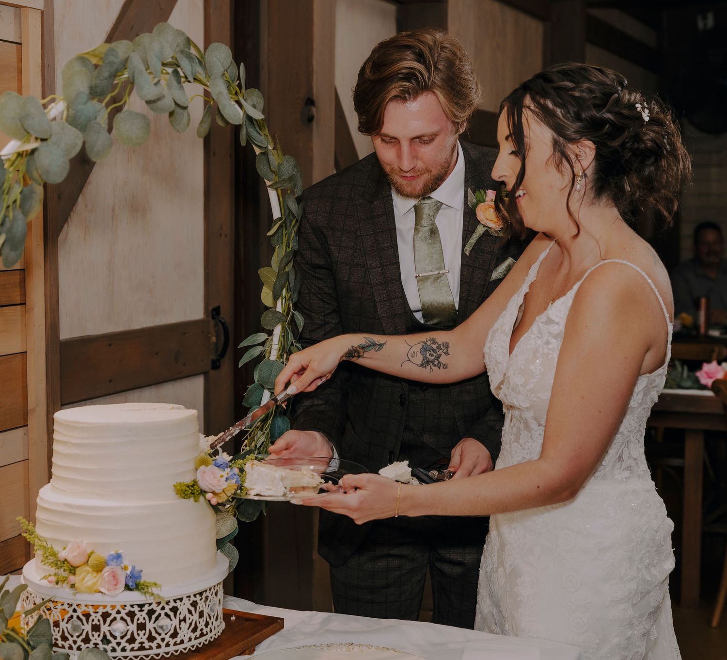 Bride and groom cutting their white wedding cake together at a rustic indoor reception venue.