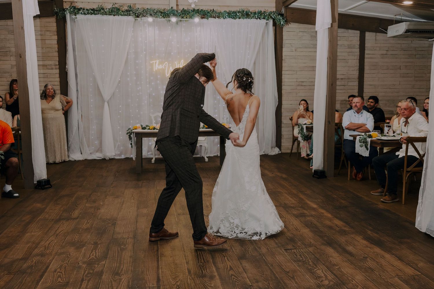 Bride and groom share their first dance on a wooden floor at an elegant indoor wedding reception venue.