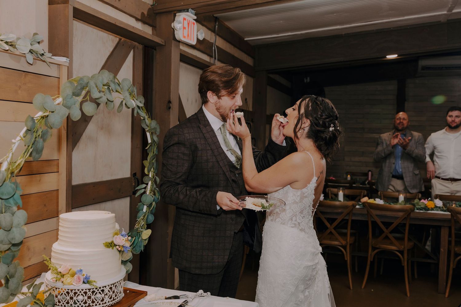 Bride and groom share a joyful cake cutting moment at their rustic barn wedding reception.