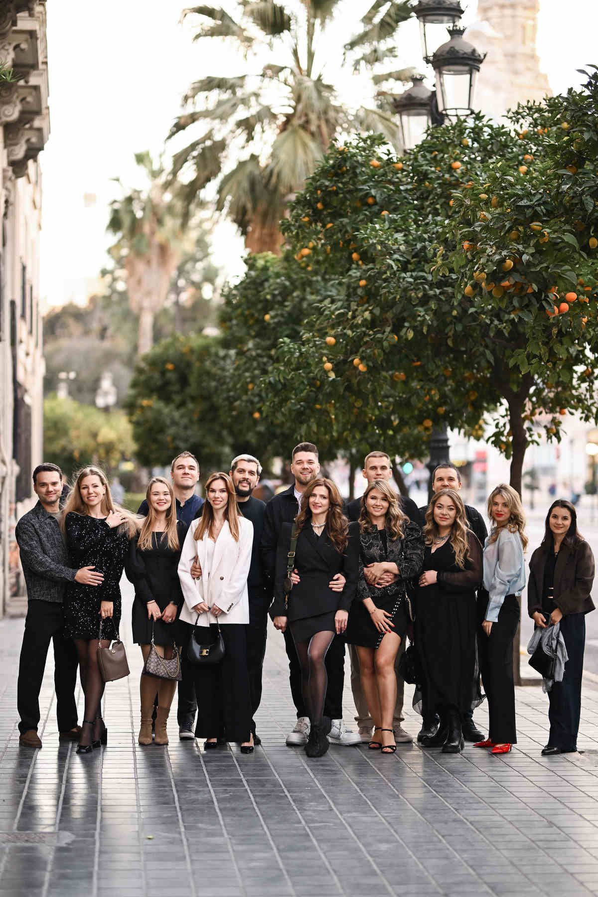 Large group portrait of stylishly dressed guests posing together on a city street during a private corporate event.